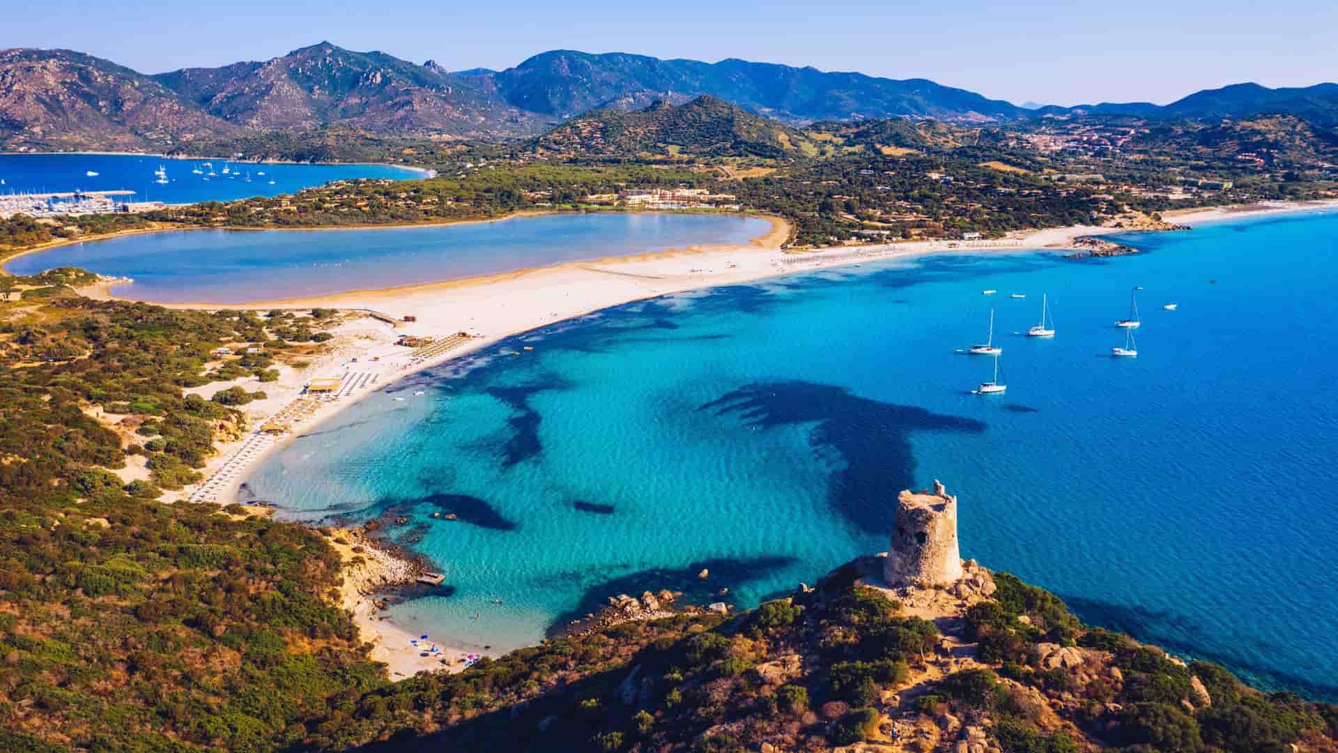 An aerial view of the stunning Spiaggia di Porto Giunco beach, near Porto Torres, with its bright turquoise water, white sand, and the historic Torre di Porto Giunco tower.