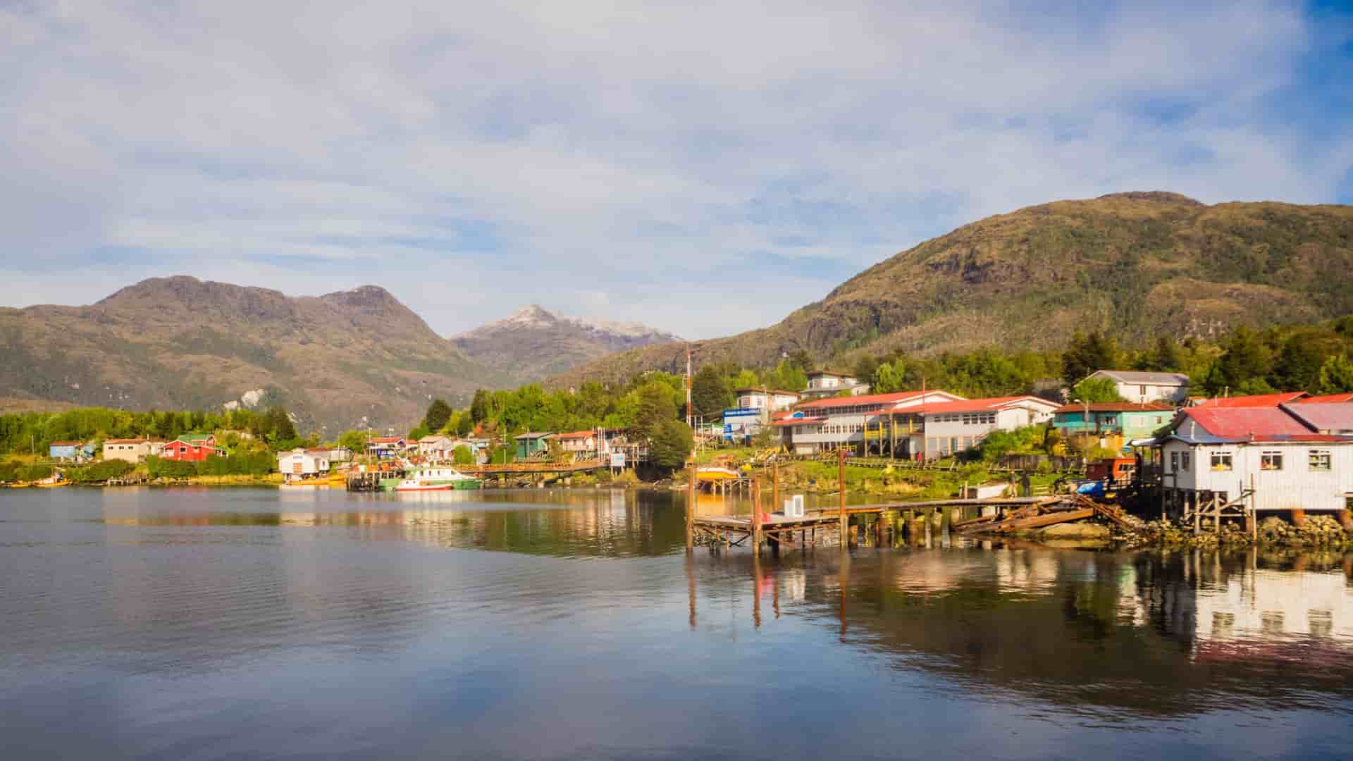Colorful houses and wooden docks line the calm waters of the settlement of Puerto Edén, Chile, nestled among green mountains.