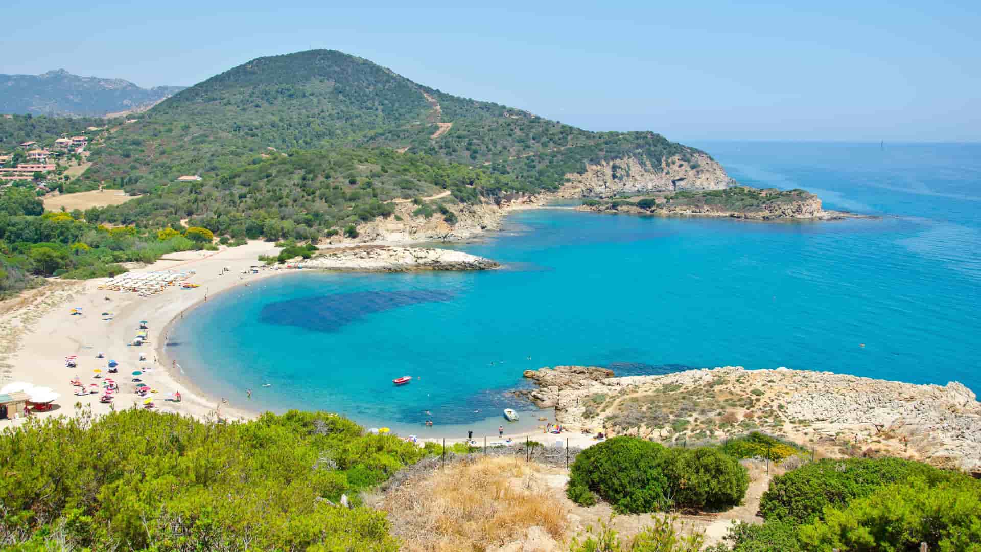 A high-angle view of a stunning crescent-shaped bay with a pristine sandy beach in Pula, Sardinia, Italy, showcasing the calm turquoise waters of the Mediterranean Sea.