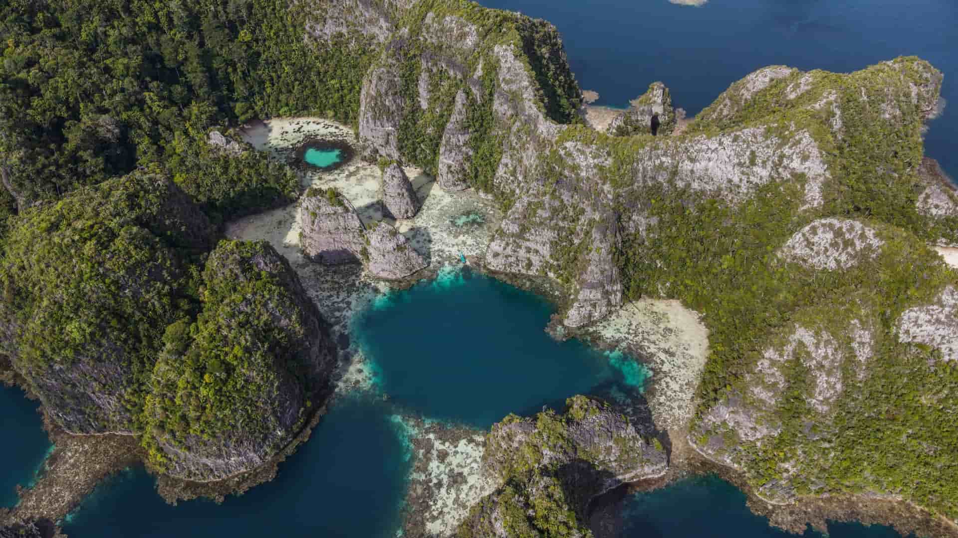 An aerial shot of the stunning natural beauty of Pulau Balbulol, Raja Ampat, showcasing limestone karst islands covered in lush vegetation surrounding a secluded, turquoise-colored lagoon.