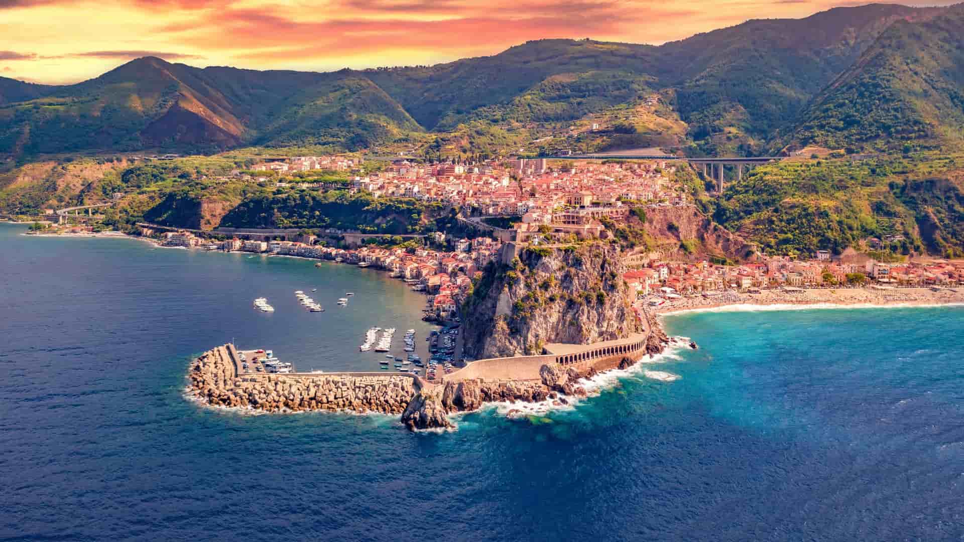 An aerial view of Scilla, a picturesque fishing village in Reggio Calabria, Italy, with colorful houses built on a rocky promontory overlooking the Mediterranean Sea and harbor.