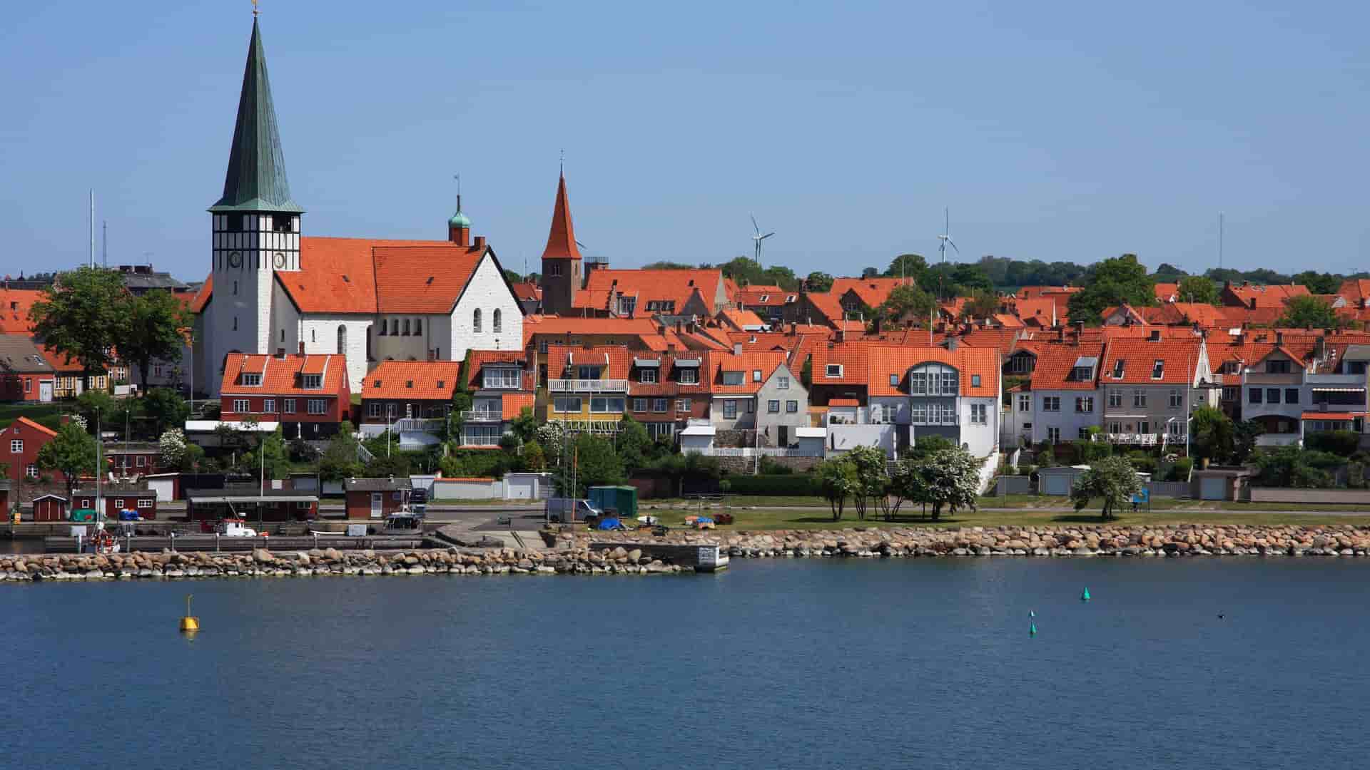 A beautiful view of the coastal town of Rønne, Denmark, featuring the iconic St. Nicolai Church and a skyline of red-roofed buildings along the waterfront.