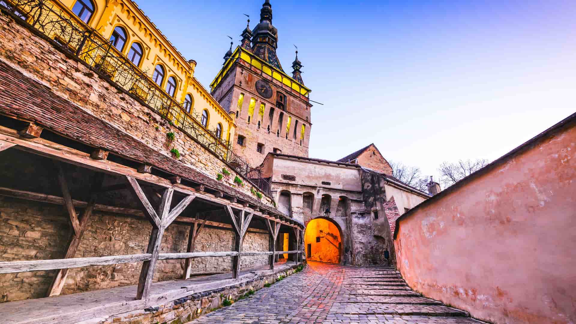 A view of the medieval city of Sighisoara, Romania, with the iconic Clock Tower and historic cobbled streets under a beautiful evening sky.