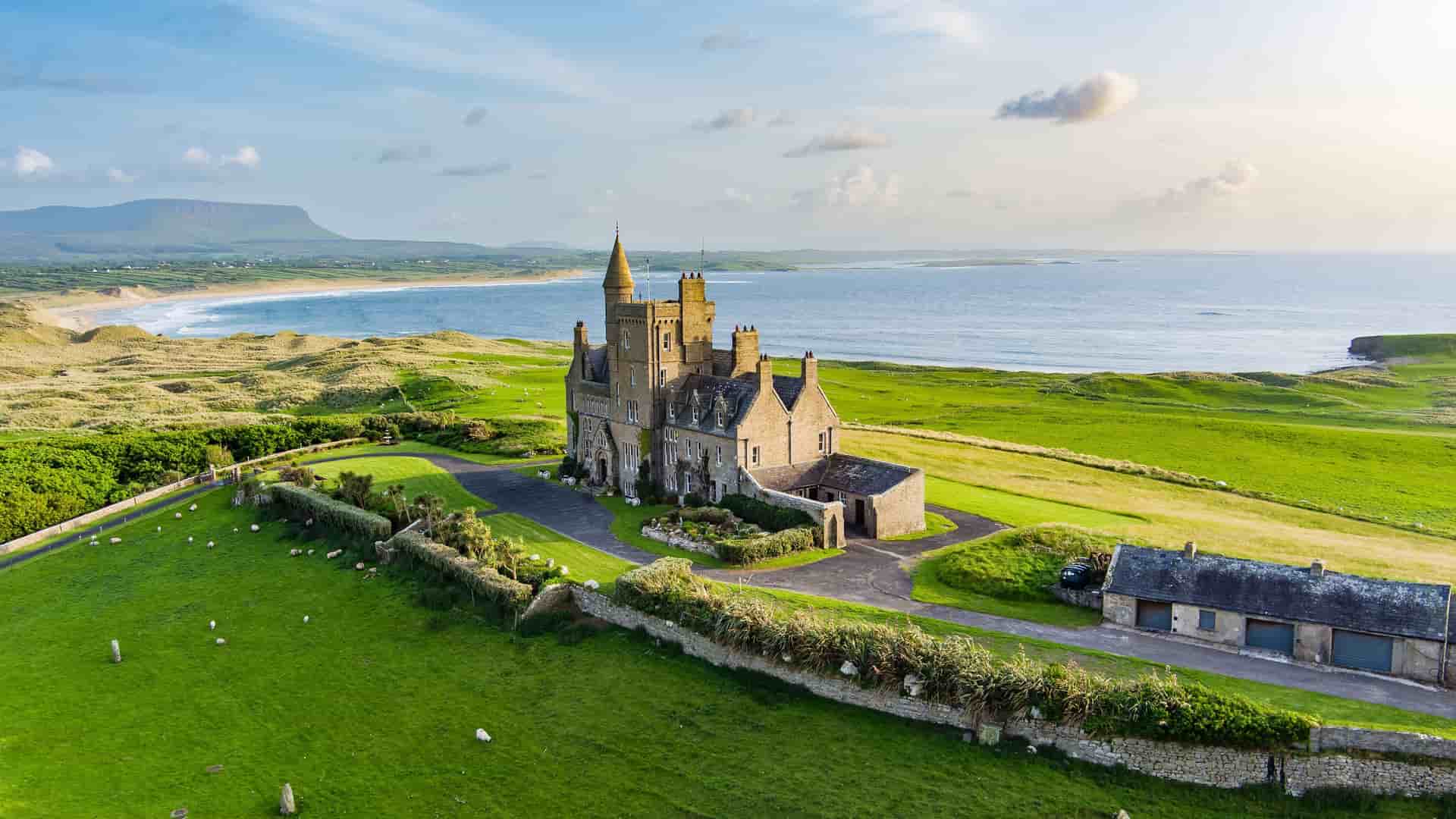 "An aerial view of the iconic Mullaghmore Castle in Sligo, Ireland, a historic castle on a lush green hilltop overlooking the Atlantic Ocean.  "