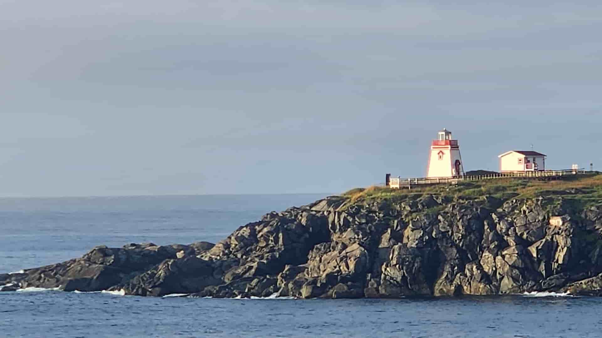 A picturesque view of a red and white lighthouse on a rocky cliff overlooking the vast Atlantic Ocean in St. Anthony, Newfoundland and Labrador.