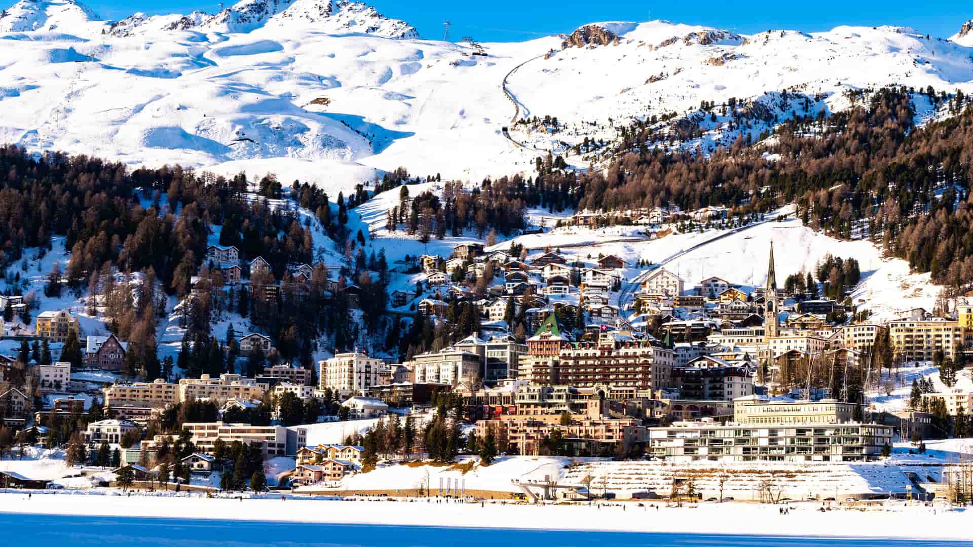A beautiful view of the luxurious resort town of St. Moritz, Switzerland, with its elegant hotels and buildings nestled at the base of the snow-covered Alps.