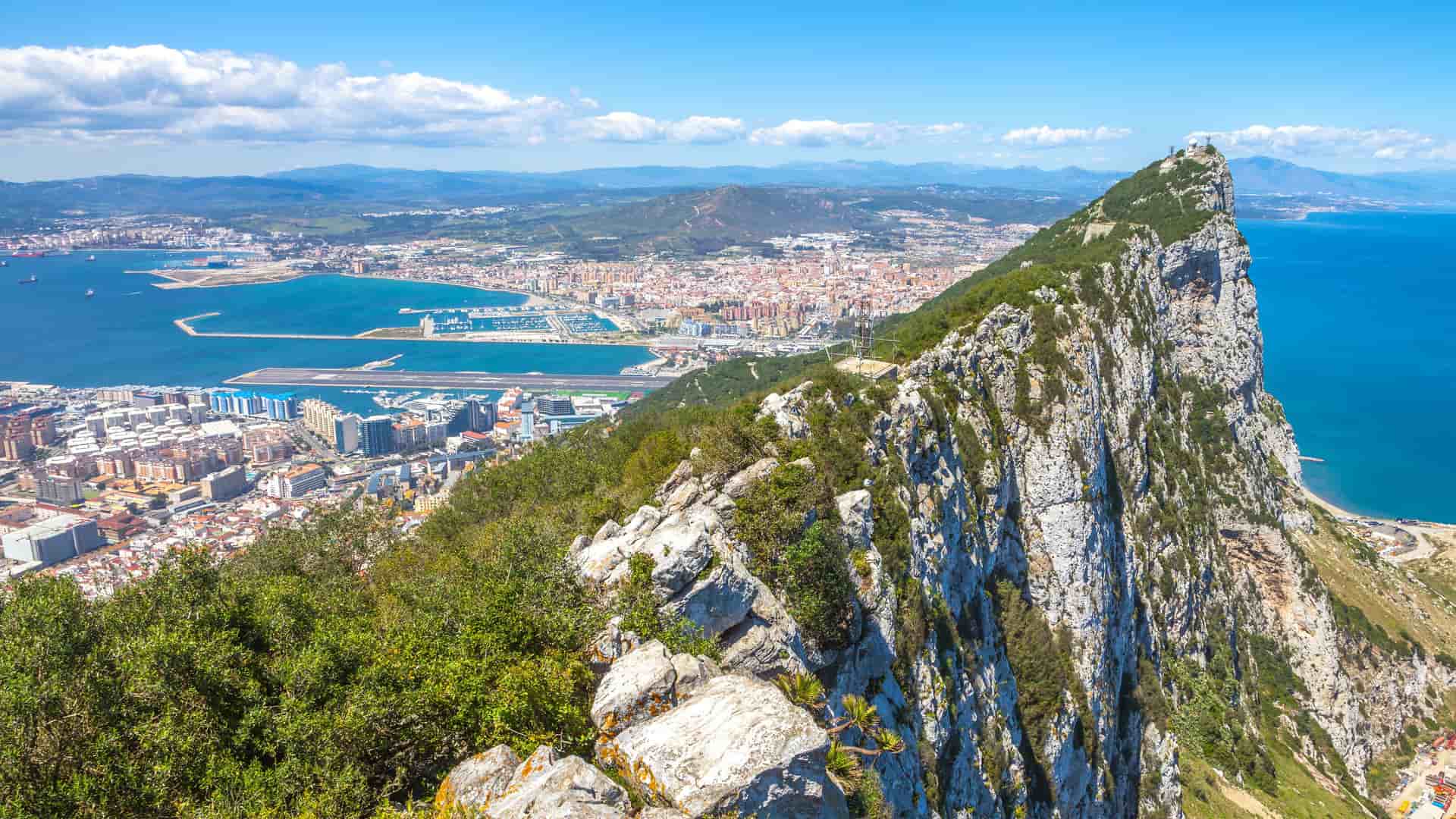 A breathtaking view of the Strait of Gibraltar from the Rock of Gibraltar, showing the bustling port and city below, with the deep blue sea in the distance.