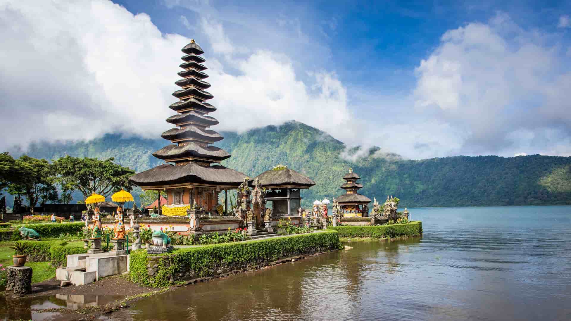 "A picturesque view of the Ulun Danu Beratan Temple in Ubud, Indonesia, with its multi-tiered pagoda reflecting on the calm lake, surrounded by manicured gardens and lush green mountains.  "