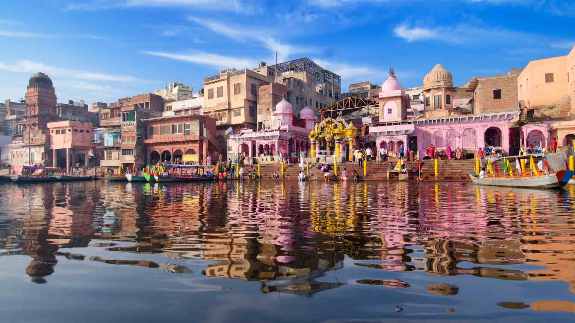 "A colorful daytime shot of the ghats in Varanasi, India, with historic buildings and temples in various shades of pink and orange along the banks of the Ganges River.  "