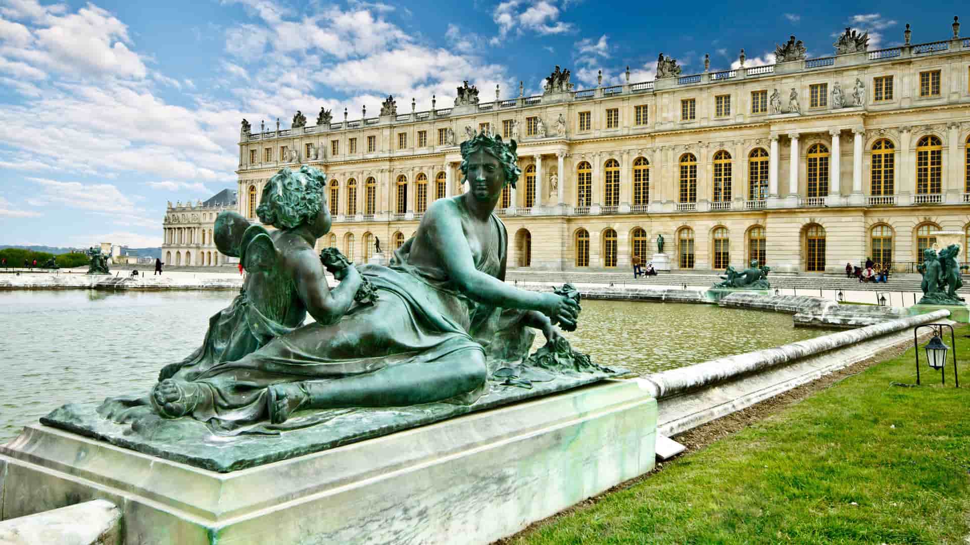 A beautiful view of a large bronze statue of two figures on the shore of a pond in the gardens of the magnificent Palace of Versailles, a UNESCO World Heritage Site near Paris.