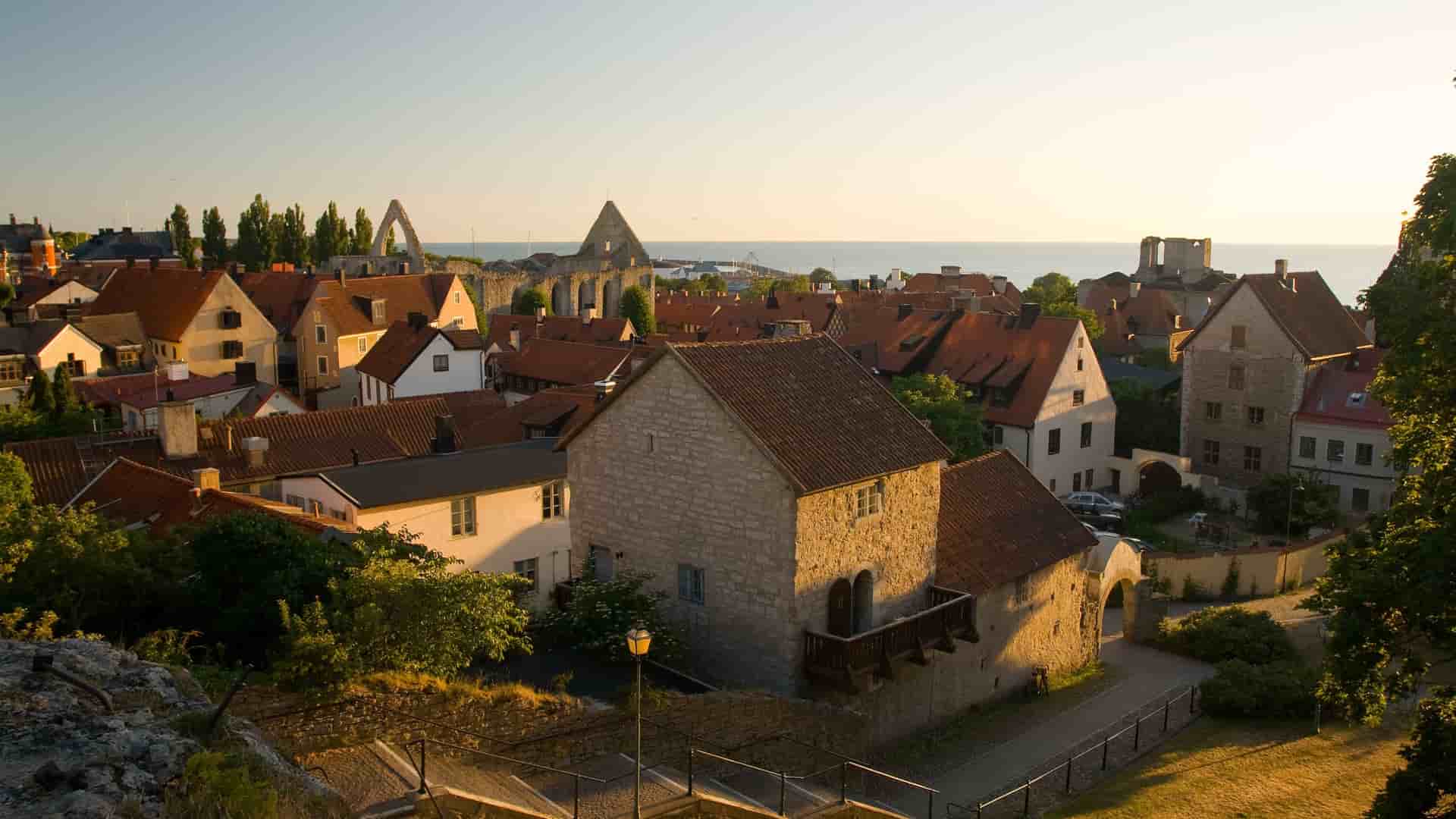 A sunset view of the medieval city of Visby, Sweden, with the red rooftops of historic houses and the sea in the distance.