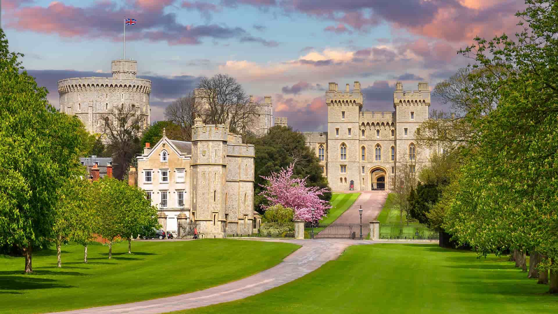 "A scenic view of the majestic Windsor Castle, the oldest and largest occupied castle in the world, surrounded by a lush green lawn with blossoming trees in Windsor, England.  "