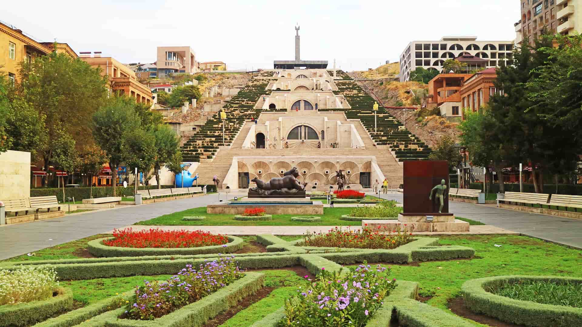 "A scenic view of the massive Yerevan Cascade complex in Armenia, with its large stone stairways, multiple levels of fountains and sculptures, and landscaped gardens in the foreground."