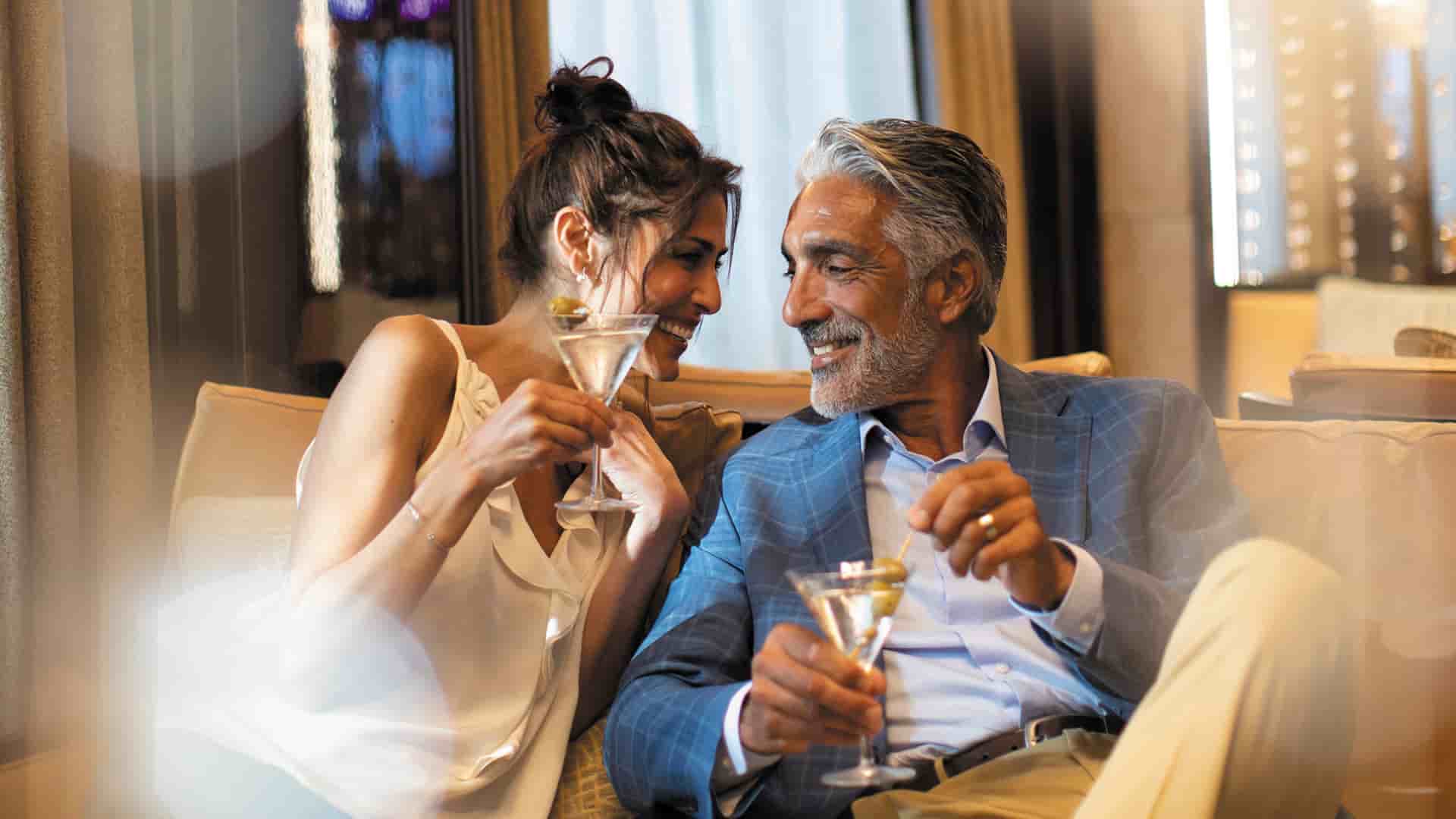 A happy couple enjoys cocktails in the elegant Horizon Lounge aboard a Regent Seven Seas luxury cruise ship.