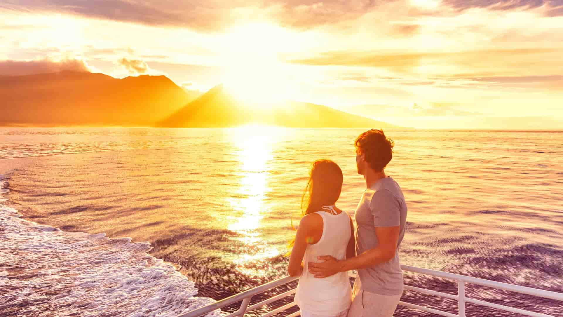 couple standing at the edge of a ship's deck at sunset
