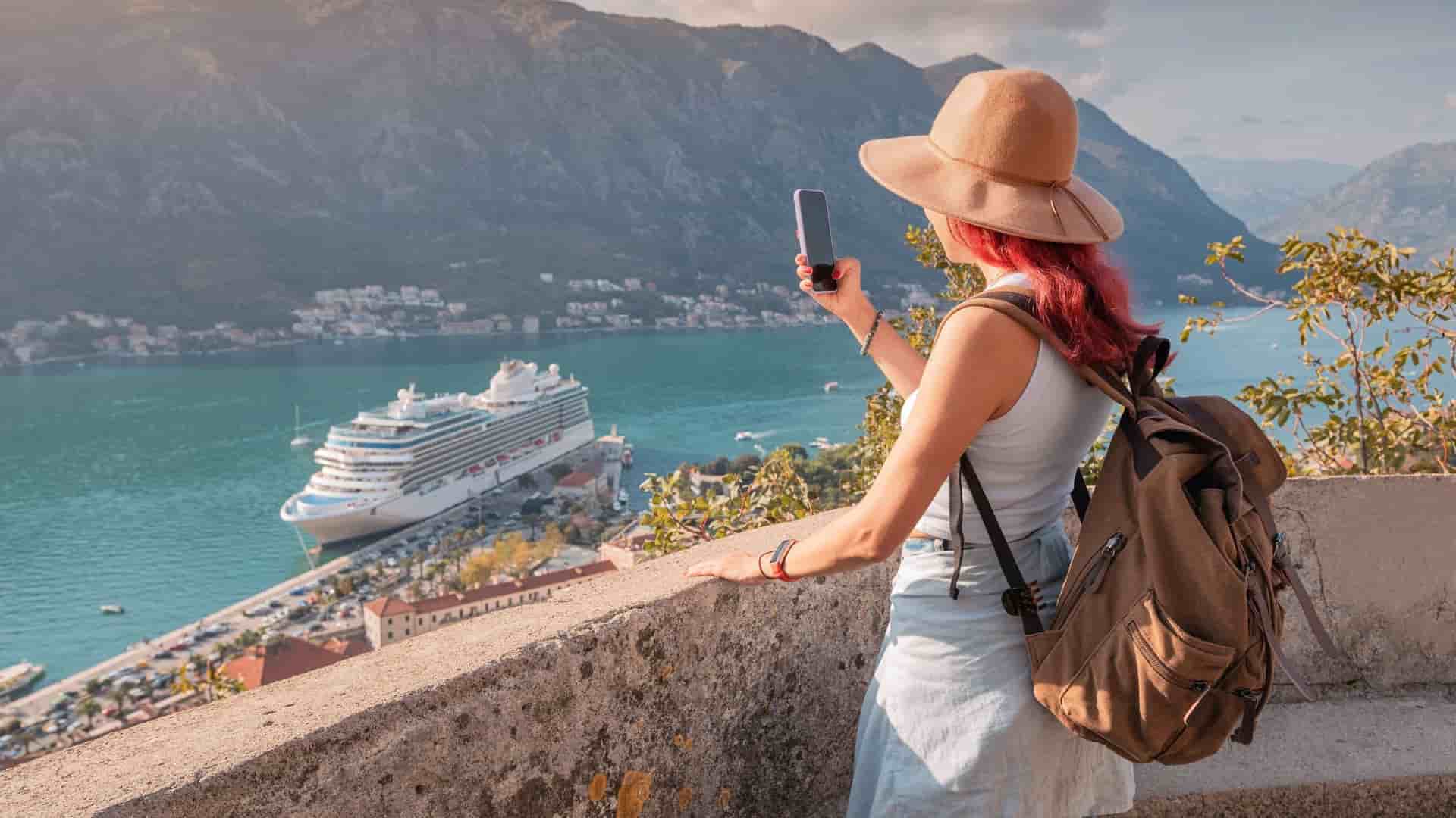 Solo traveller taking a picture overlooking mountains and a cruise ship.