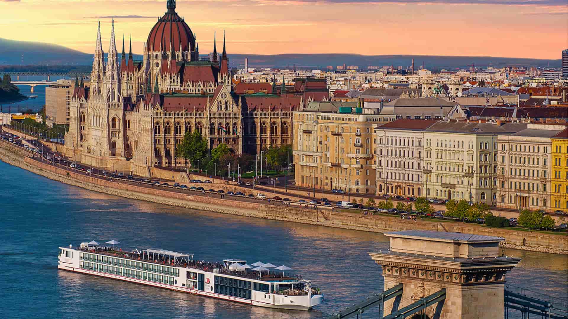 Viking long ship sails through Budapest, Hungary with a glowing skyline and city in the background.