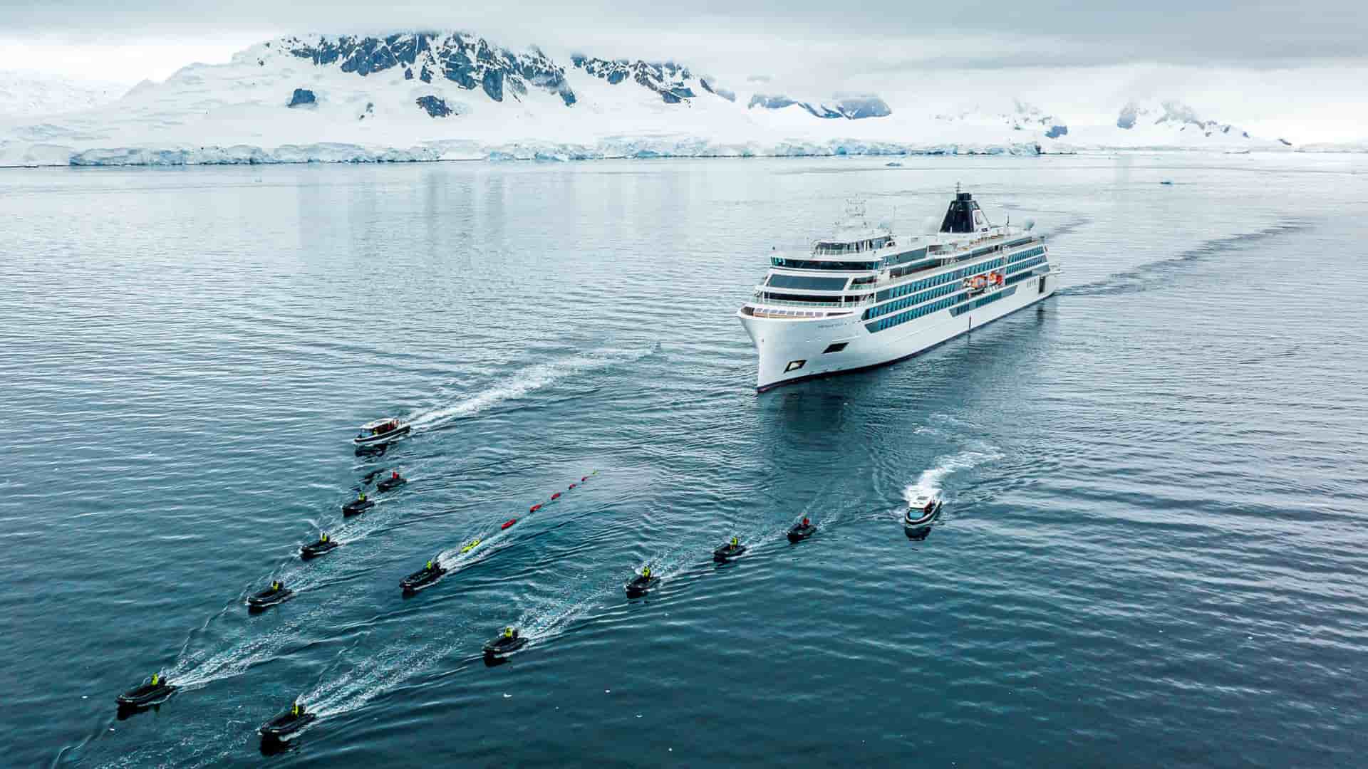 Viking Octantis ship sailing through icy waters off the coast of Antarctica, with a fleet of Zodic boats departing for an exciting shore excursion.