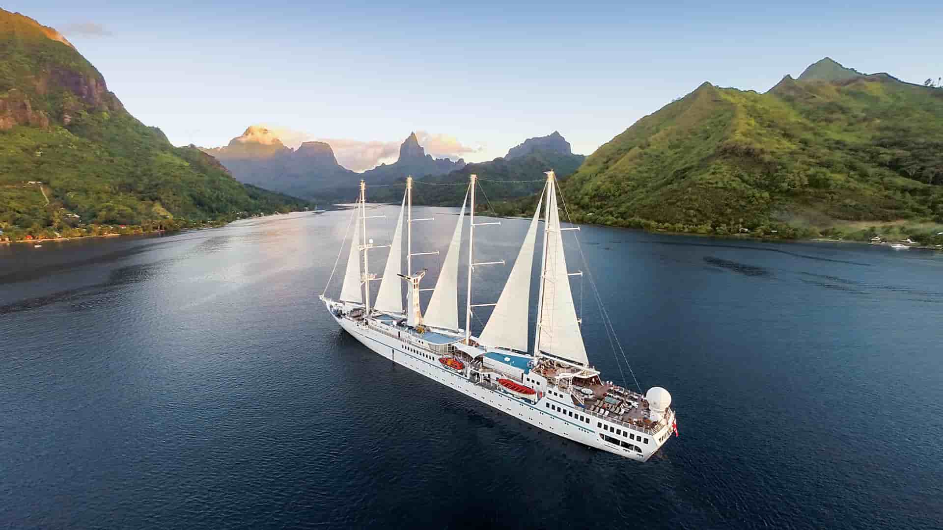 A Windstar sailing yacht cruises through the stunning tropical bay of Moorea, French Polynesia, with majestic volcanic mountains in the background.