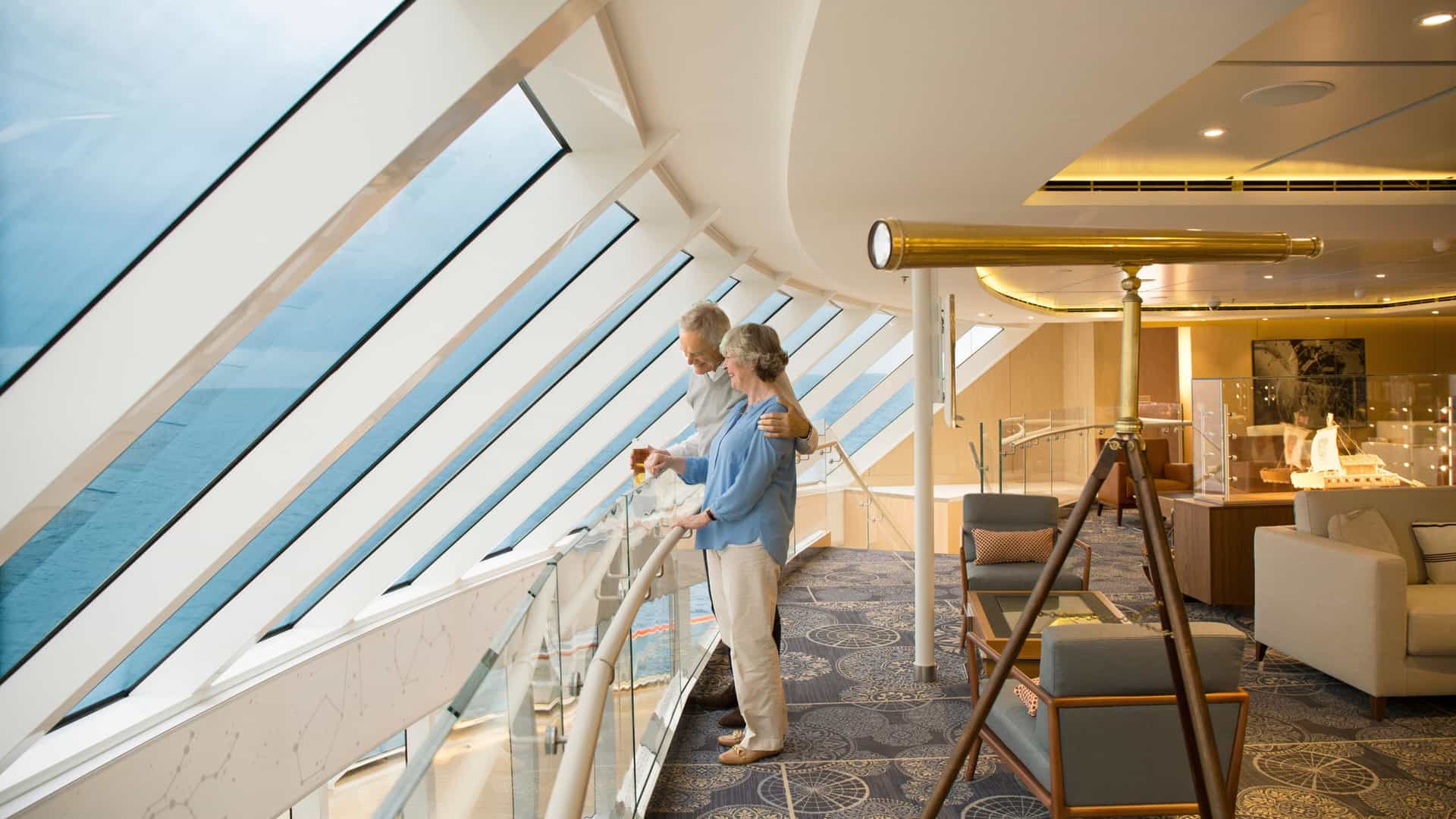 Couple standing together looking out a large floor to ceiling window in the Explorers Lounge on a Viking cruise.