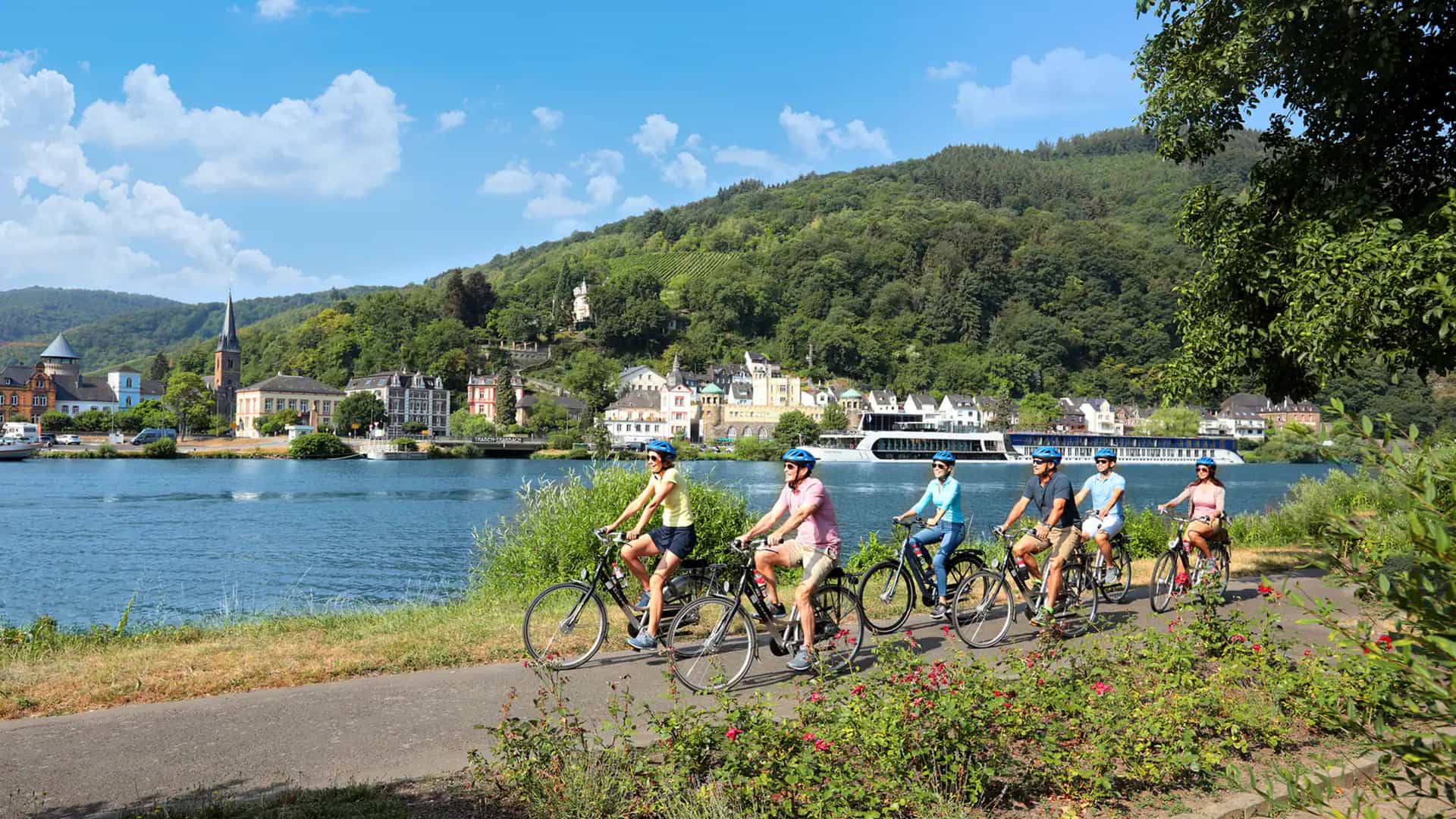 A group of people biking along a scenic path next to a European river.