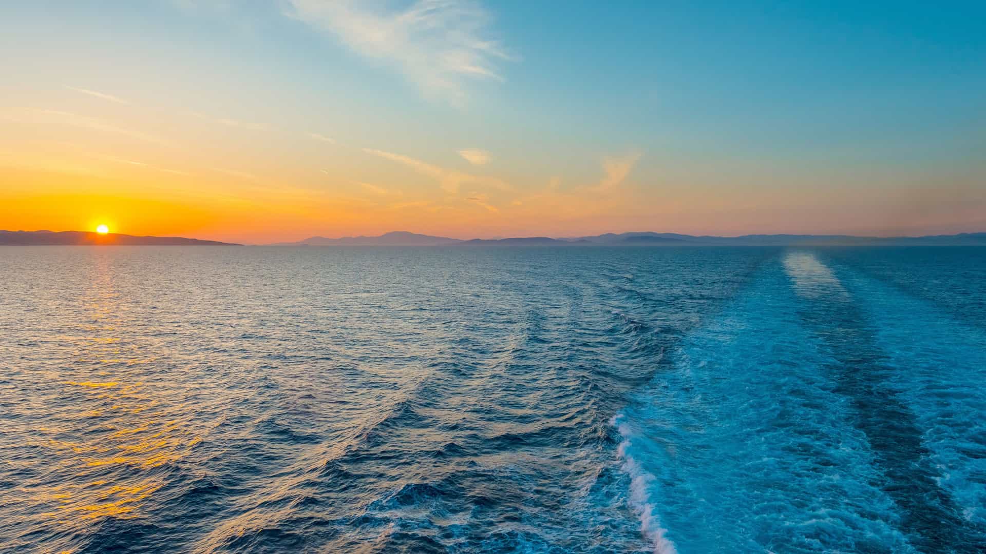 A serene sunset over the open ocean, showing the wake of a ship, representing tranquil sea days on a Trans-Atlantic Azamara cruise.