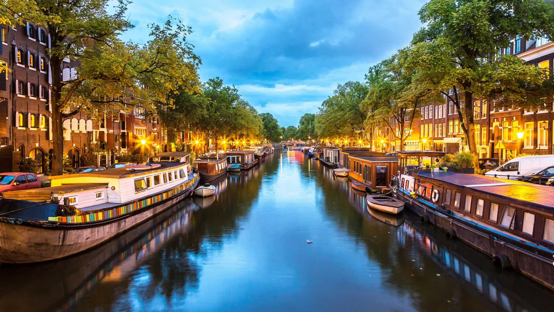 Evening view of Amsterdam canal with historic houses, houseboats, and illuminated bridges, a popular Carnival Northern Europe cruise stop.