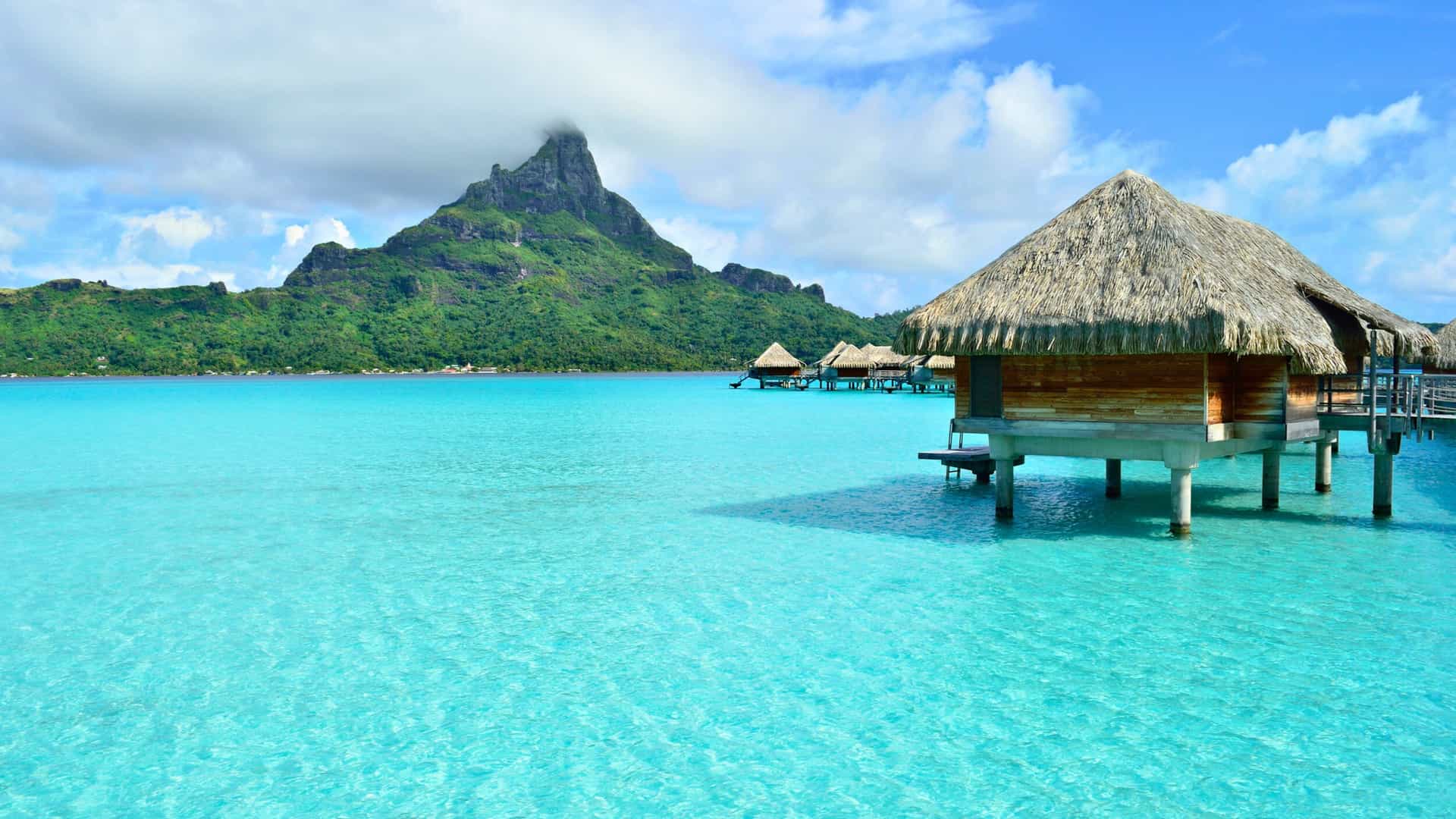 Overwater bungalows in Bora Bora, Tahiti, French Polynesia, with Mount Otemanu and turquoise lagoon; a luxurious Carnival South Pacific cruise destination.