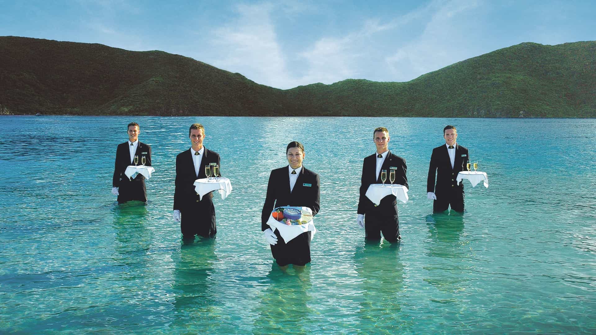 Five members of Seabourn's staff in suits standing in the water holding trays for the signature Caviar in the Surf event.