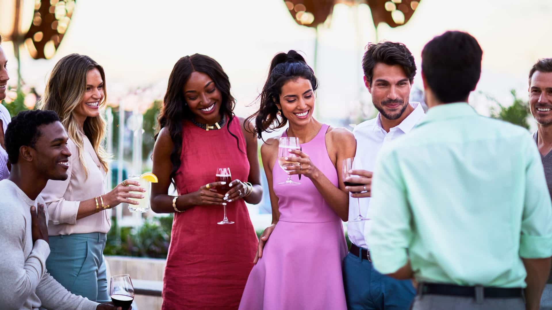 A diverse group of friends smiling and holding drinks while socializing at an outdoor rooftop garden party.