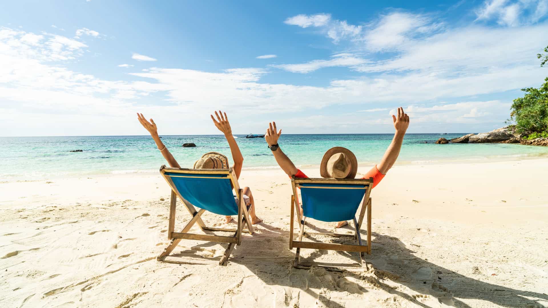 A couple sitting on beach chairs with their hands up, looking at the ocean shore.