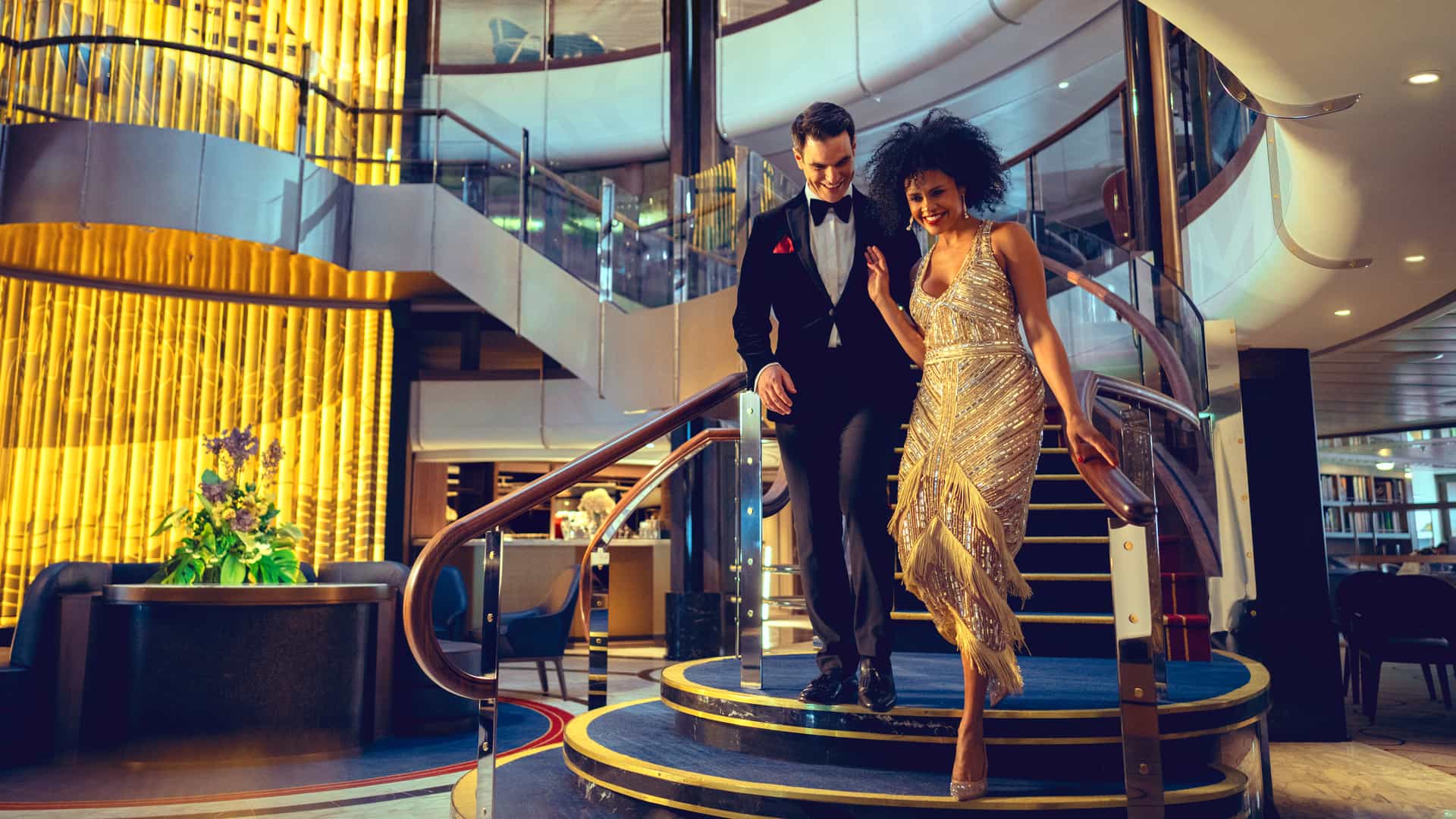 A couple dressed in formal attire walking down a glamourous, grand staircase during a formal night onboard a Cunard cruise.
