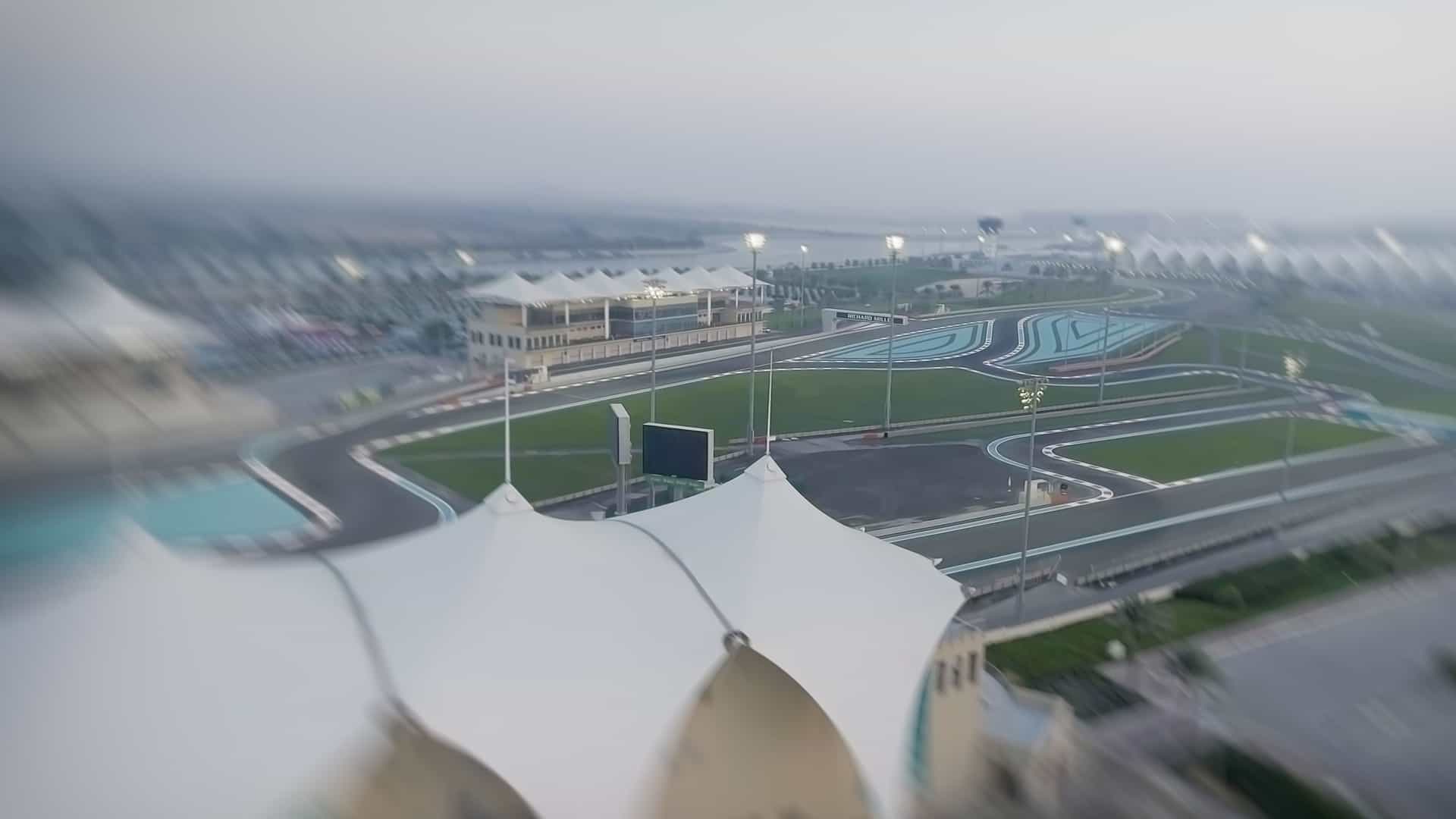 Aerial view of Ferrari World on Yas Island, Abu Dhabi, UAE. The massive theme park features the distinctive, low-slung red roof with the iconic yellow and black Ferrari logo, surrounded by roads and adjacent structures.