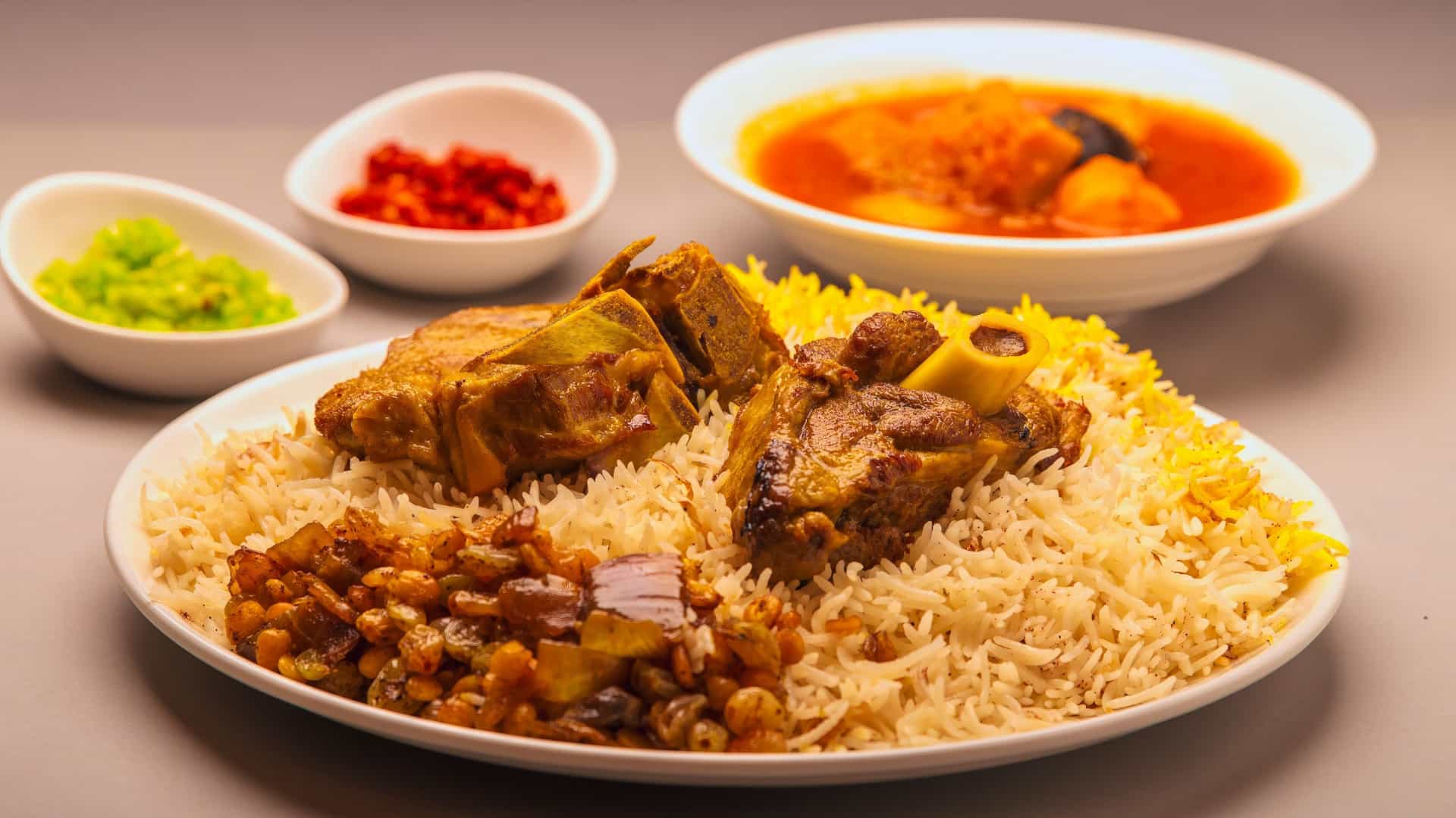 A generous portion of the traditional Arabian meal, Lamb Machboos or Lamb Mandhi. The dish features tender, slow-cooked seasoned lamb (or mutton) served atop a large bed of aromatic spiced rice, garnished with nuts and raisins.