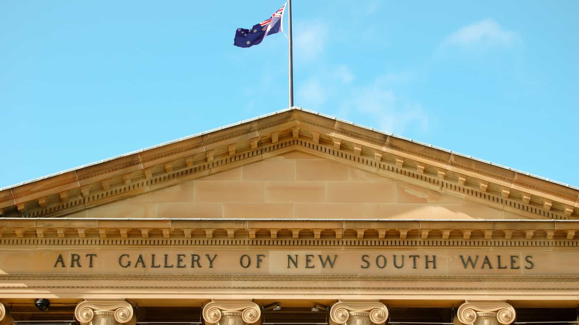 The grand Neoclassical exterior and entrance of the Art Gallery of New South Wales, located in The Domain, Sydney, Australia. The public art gallery features large columns and stone steps leading to the main portico.