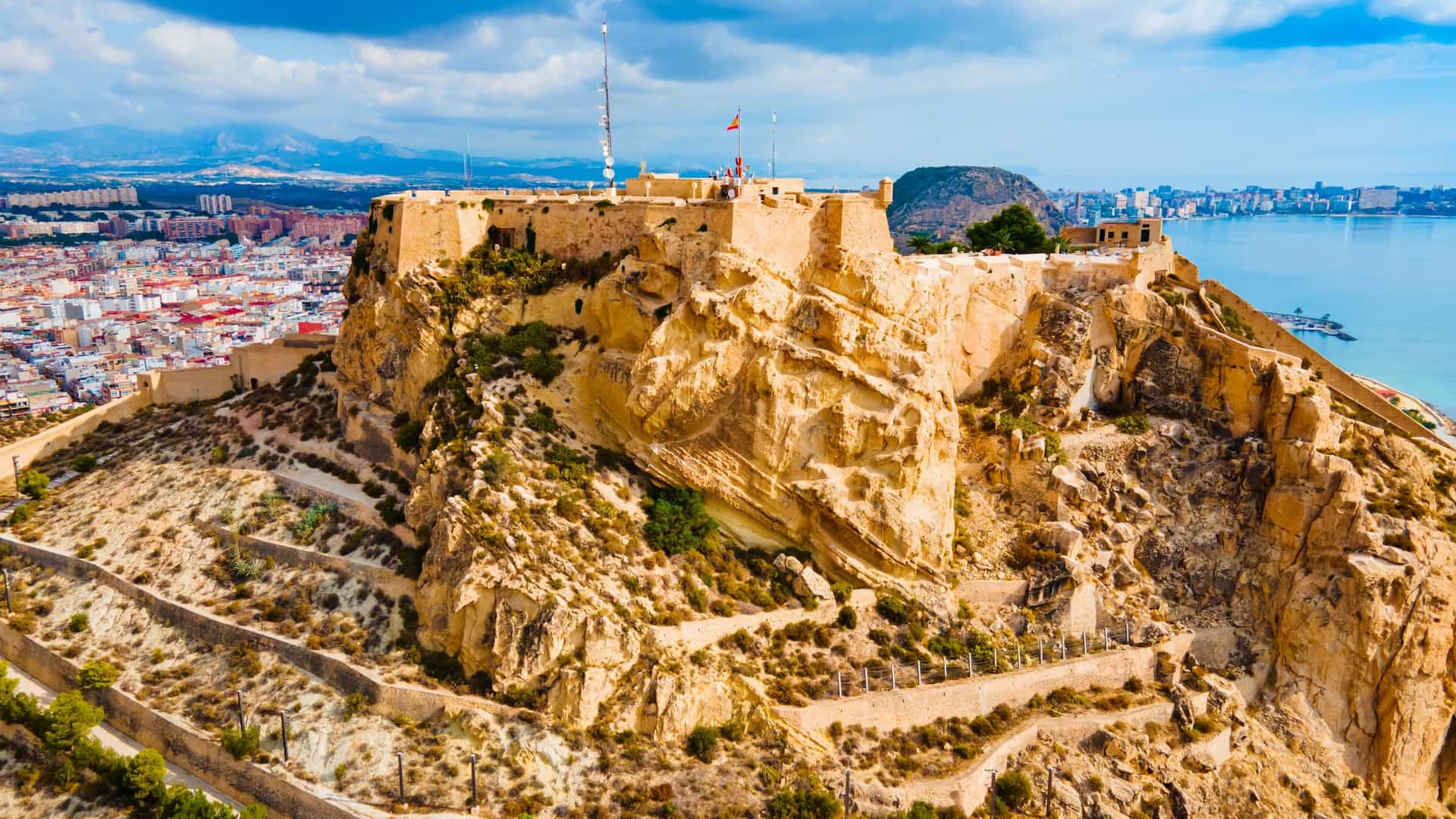 An aerial panoramic view of Santa Bárbara Castle (Castillo de Santa Bárbara) in Alicante, Spain, showcasing the massive fortress perched atop Mount Benacantil overlooking the city and the Mediterranean Sea.