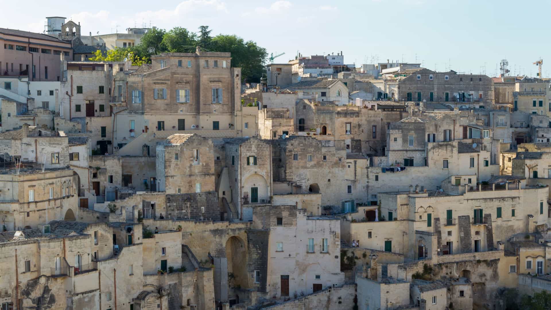 A beautiful, sunlit view of a narrow, colorful street in the Old City (likely in a Mediterranean location), with stone archways and historic architecture.