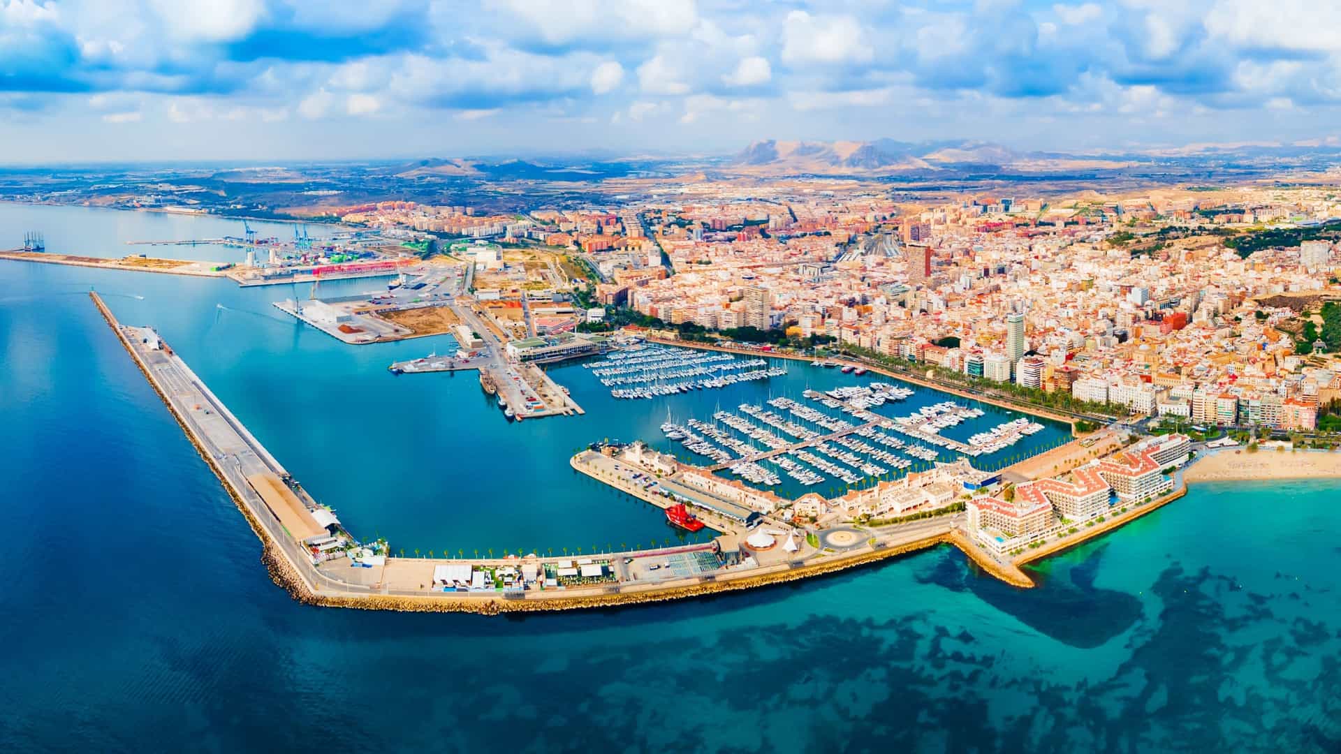 An aerial view of the Alicante City Port in Spain, showing a large number of moored boats and yachts against the blue of the Mediterranean Sea.