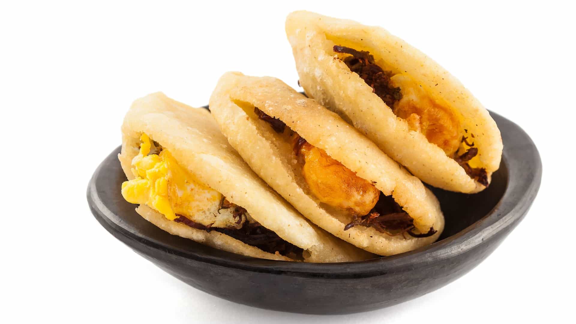 A close-up of an Arepa de Huevo, a traditional Colombian fried cornmeal cake. The golden-brown, crispy arepa has been cut open to reveal its filling of a whole fried egg and shredded meat inside, served likely as a breakfast or snack.