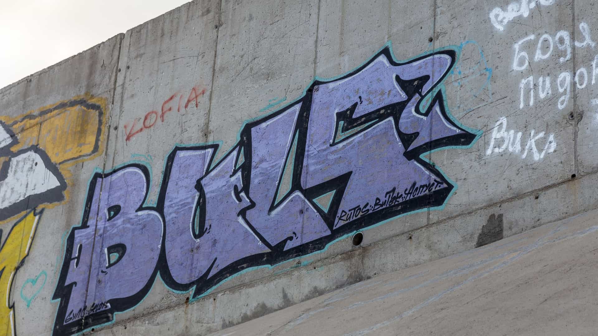 A close-up, abstract detail of vibrant street art graffiti from the Barrio Abajo neighborhood of Barranquilla, Colombia. The image shows layers of spray paint, drips, and marks in various colors, including white, black, blue, pink, and yellow, covering a textured surface or wall, embodying modern urban culture.