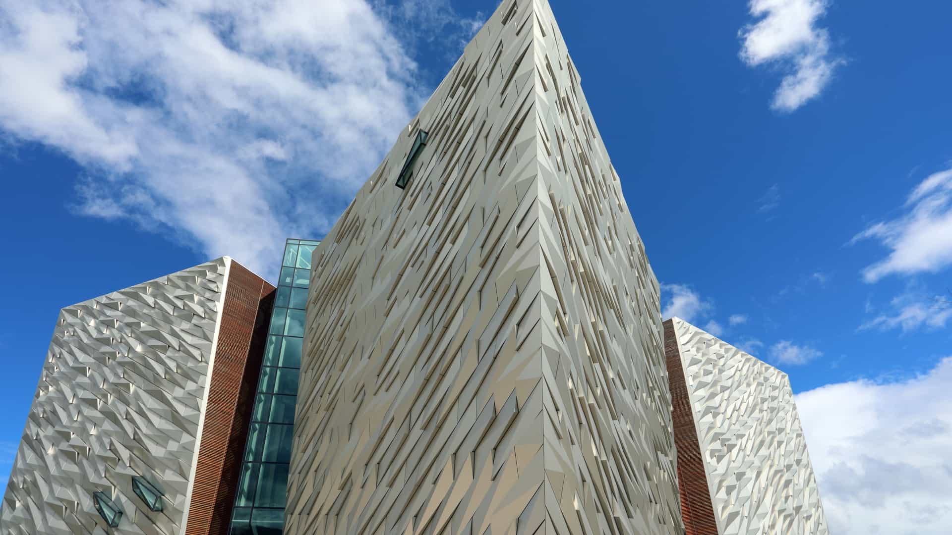  The modern, angular, silver clad exterior of the Titanic Belfast museum building, located in the Titanic Quarter, Belfast, Northern Ireland, under a cloudy sky. The building's unique architecture is designed to evoke the shape of ship hulls.