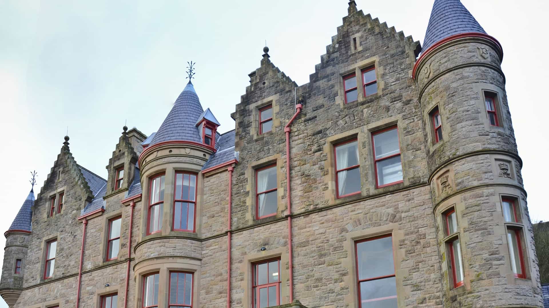  A view of Belfast Castle, a Victorian mansion built in the Scottish Baronial style, located on the slopes of Cave Hill in Northern Ireland. The stone building has towers and is surrounded by well maintained gardens and lawns.
