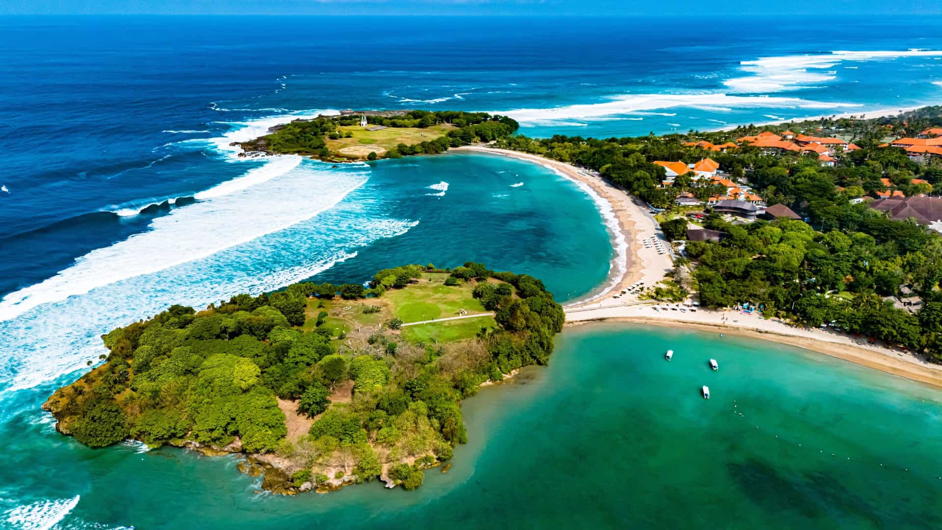  A high angle panoramic view of the Nusa Dua resort area in Bali, Indonesia. The image shows a sprawling, manicured landscape of luxury resorts with lush green gardens, swimming pools, and pristine white sand beaches bordering the turquoise ocean.