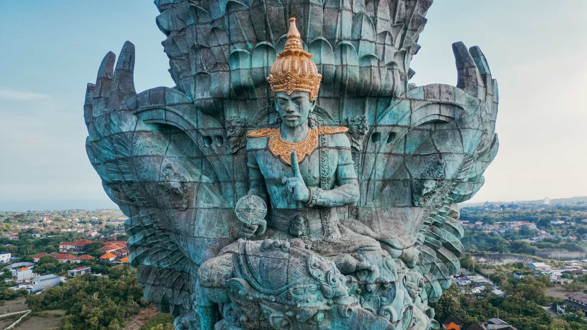  A full length photo of the massive Garuda Wisnu Kencana statue in Bali, Indonesia. The statue, standing at 122 meters tall, depicts the Hindu deity Vishnu riding on the back of the mythical bird, Garuda. The statue is made of copper and brass, and is positioned atop a large pedestal within the cultural park.