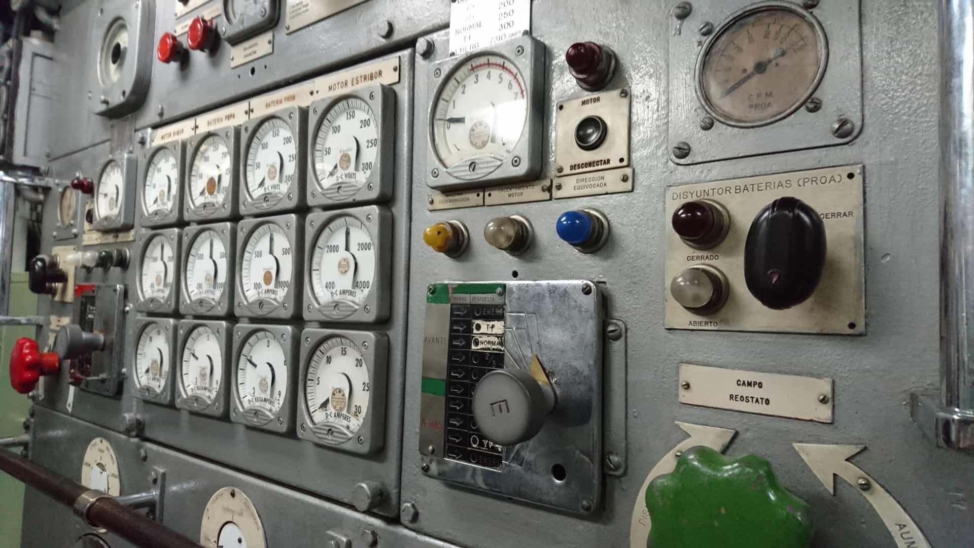 A dark, cramped, and detailed view inside the torpedo compartment of the BAP Abtao submarine, a museum ship in Callao, Peru. The metal walls are lined with complex machinery, including numerous pipes, gauges, and valves, highlighting the confined and technical environment of the historic naval vessel.