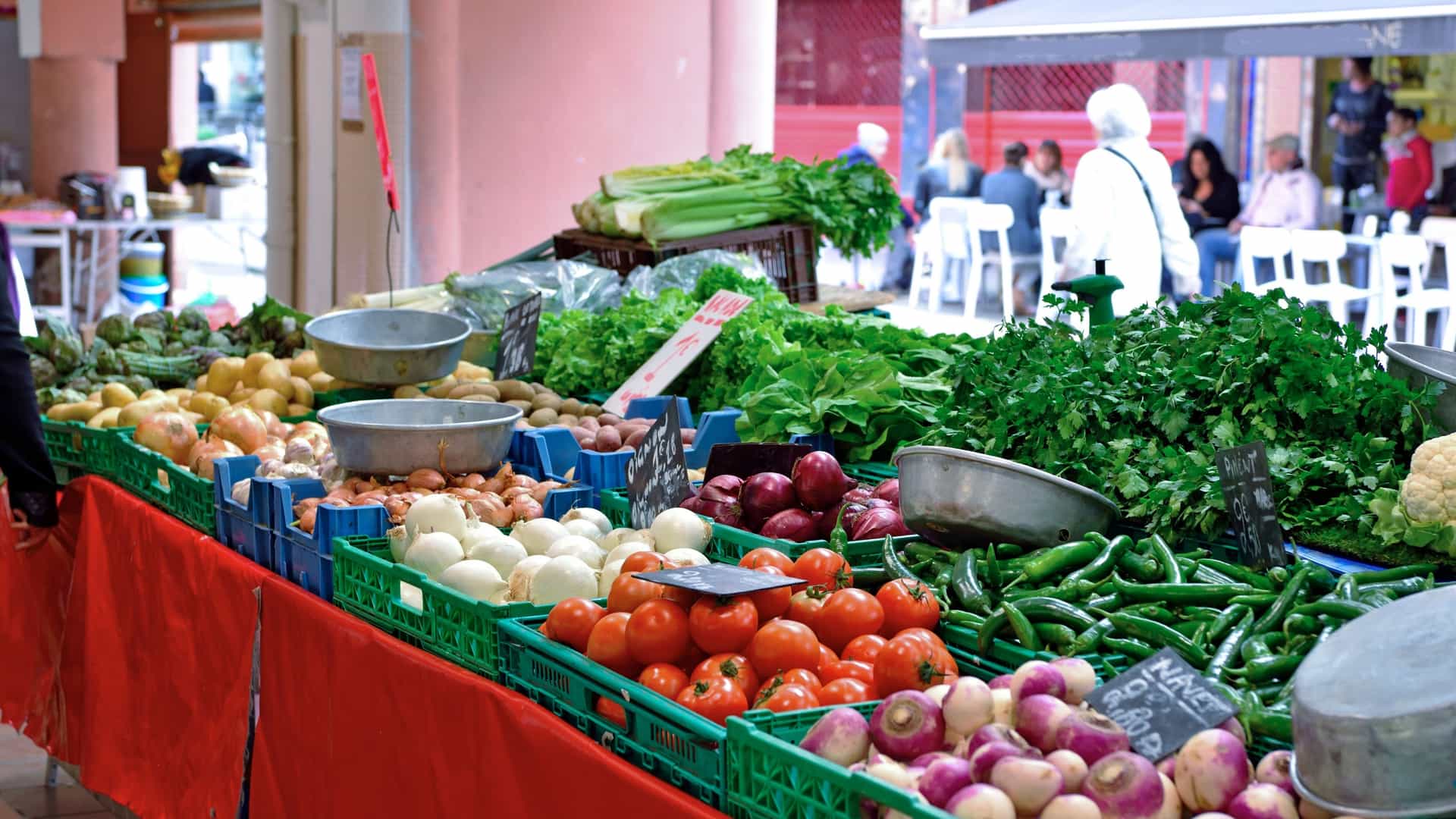 A vibrant scene at the Marché Forville in Cannes, France, a large, covered market displaying abundant fresh produce, fruits, vegetables, and local goods, with vendors and customers visible.
