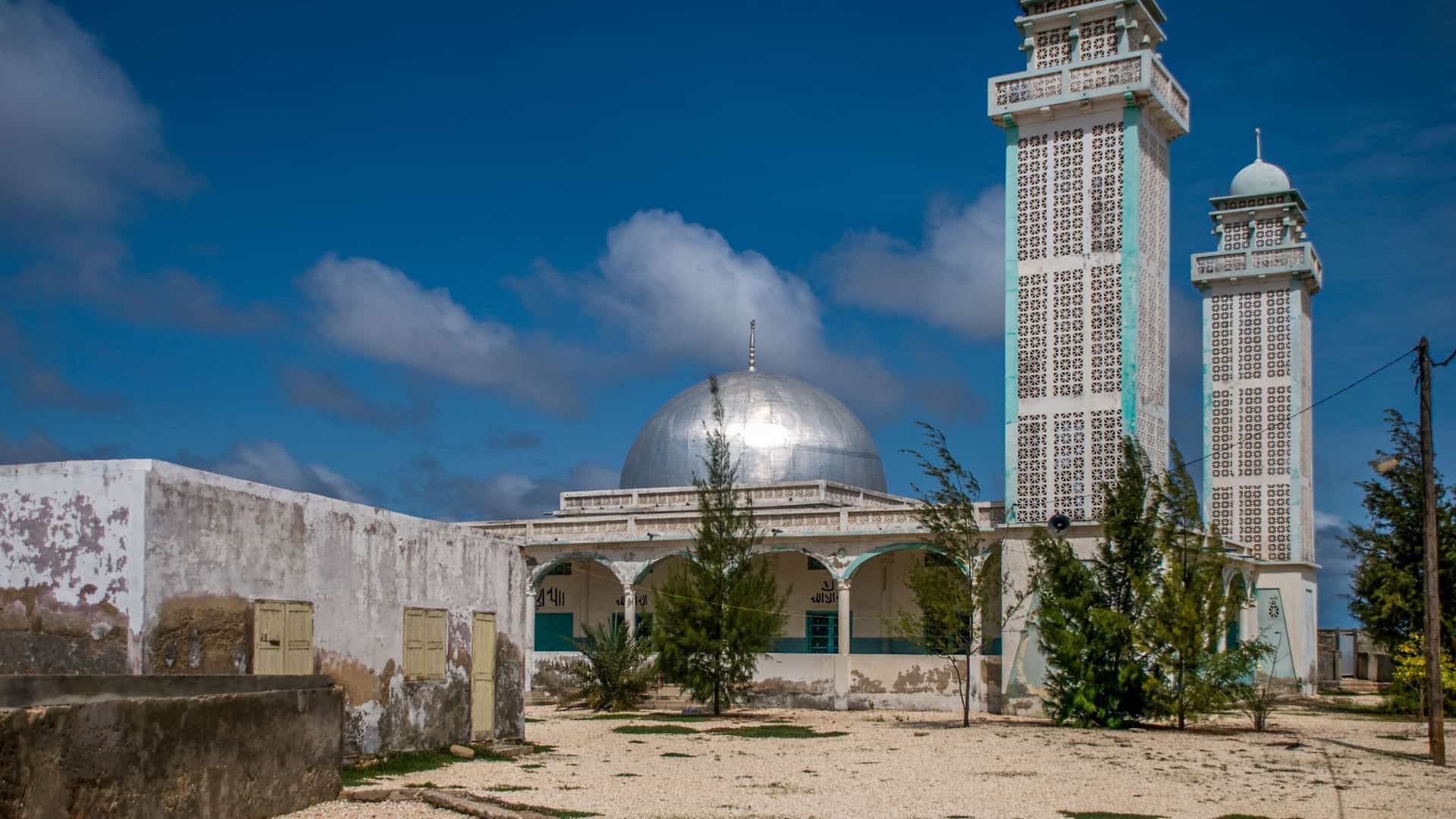A striking view of a large, modern Islamic mosque in Senegal, Africa, featuring a white facade, multiple towering minarets with green domes, and a large central dome.