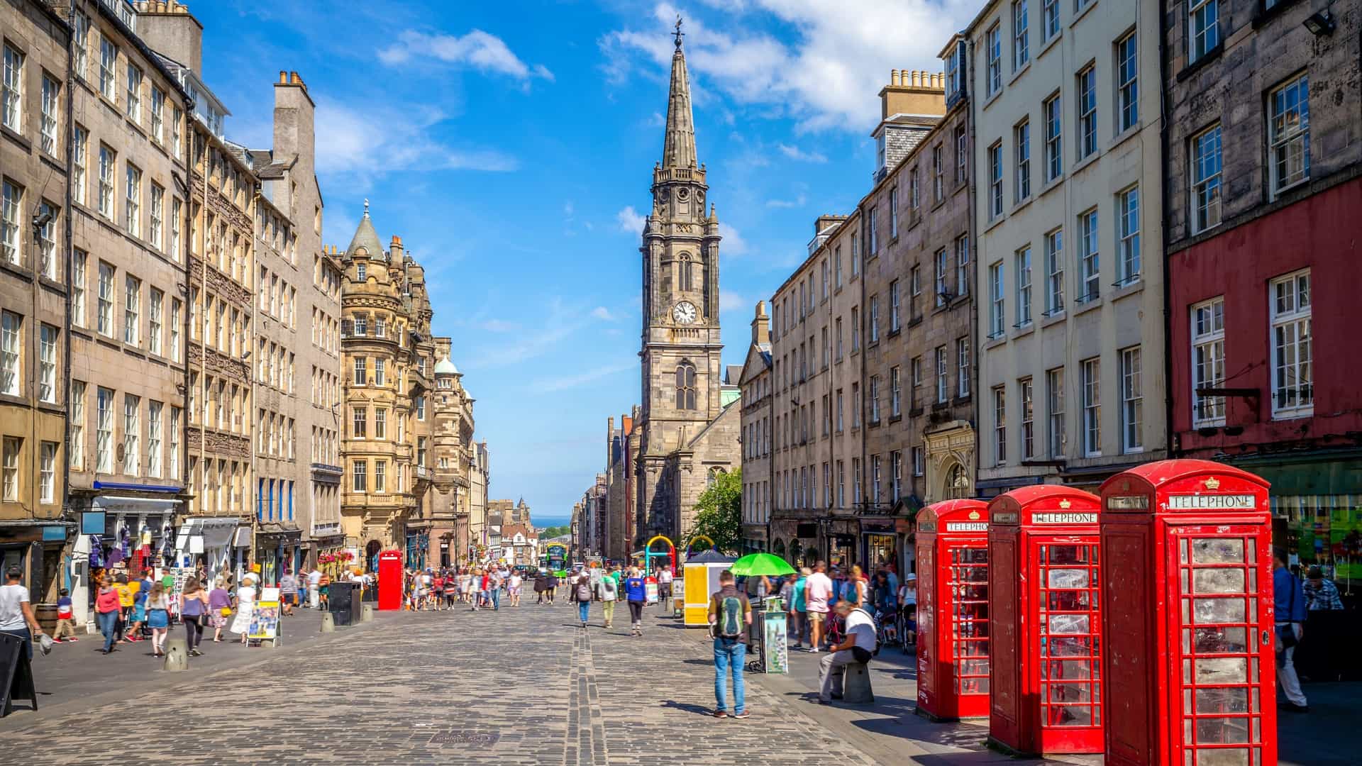  A view of the Royal Mile in Edinburgh, a cobblestone street lined with tall, historic buildings. The street is bustling with pedestrians and is a central part of the city's Old Town.