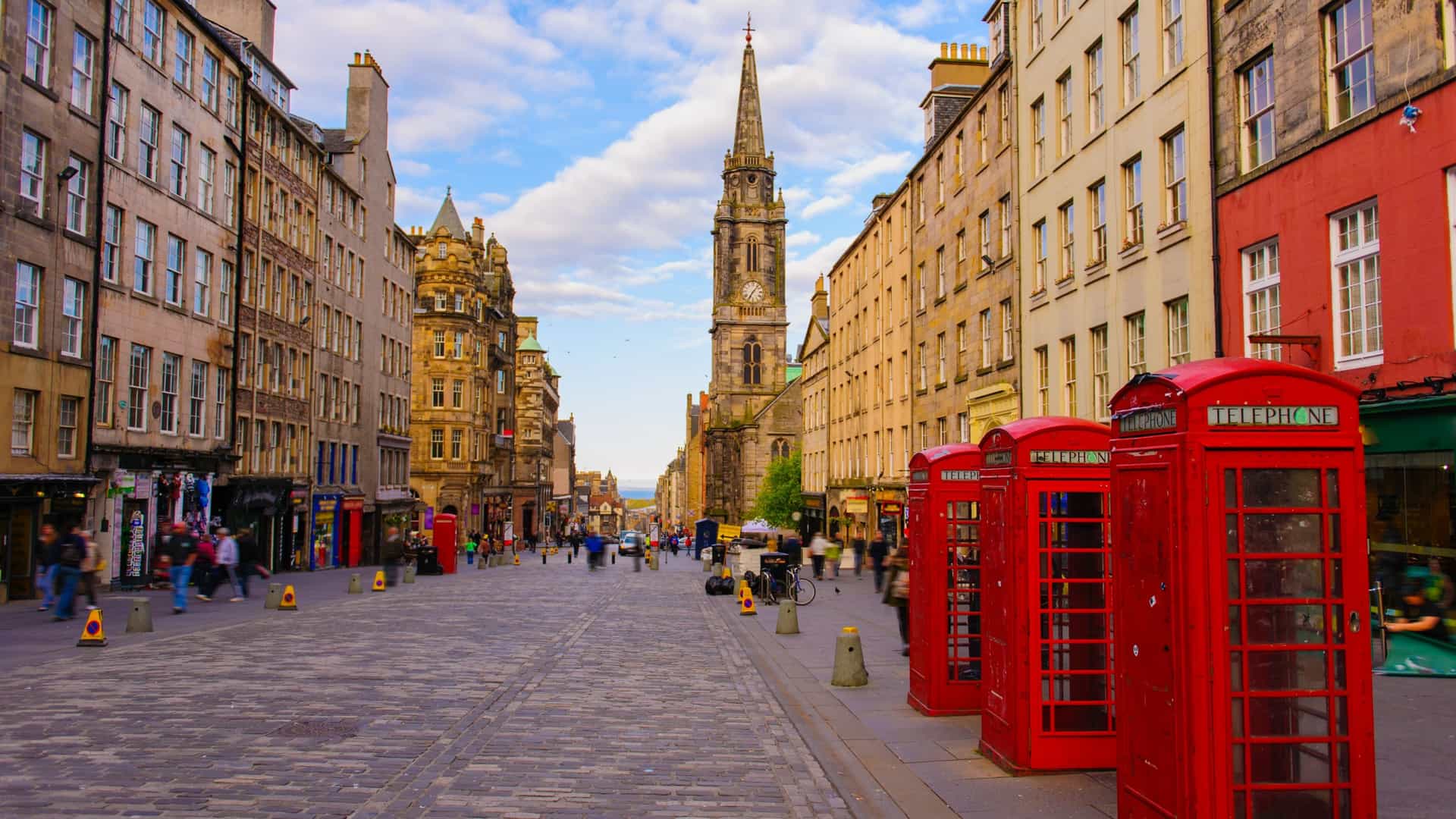  A street level view of the historic Royal Mile in Edinburgh, Scotland. The image shows a cobblestone street lined with tall, old stone buildings, typical of the city's Old Town architecture. The street is bustling with pedestrians, conveying the lively atmosphere of this famous tourist thoroughfare.