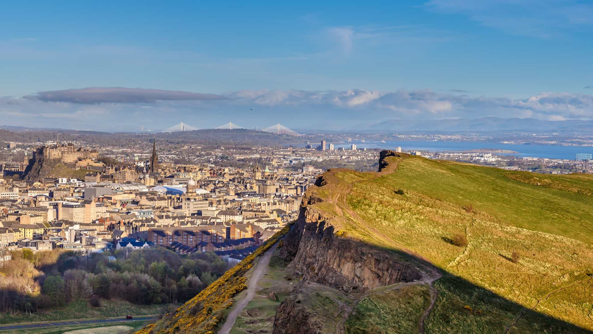  A panoramic view of Arthur's Seat, an ancient extinct volcano and the highest point in Holyrood Park, Edinburgh, Scotland. The image captures the rugged, green covered hill with its steep slopes and rocky outcrops, towering over the city. The view includes a vast sky, and the image conveys the natural, wild landscape that exists within the urban environment.